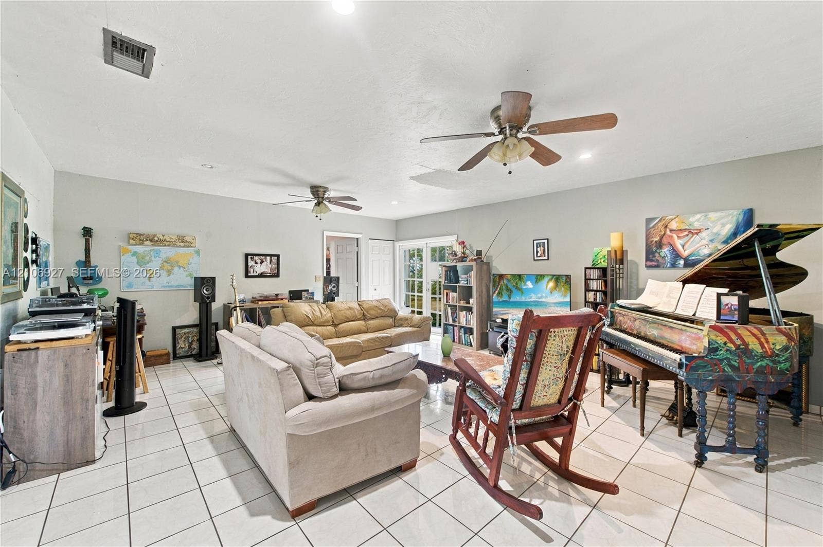 Spacious room featuring neutral-toned tile flooring, dual ceiling fans, and multi-pane glass french doors