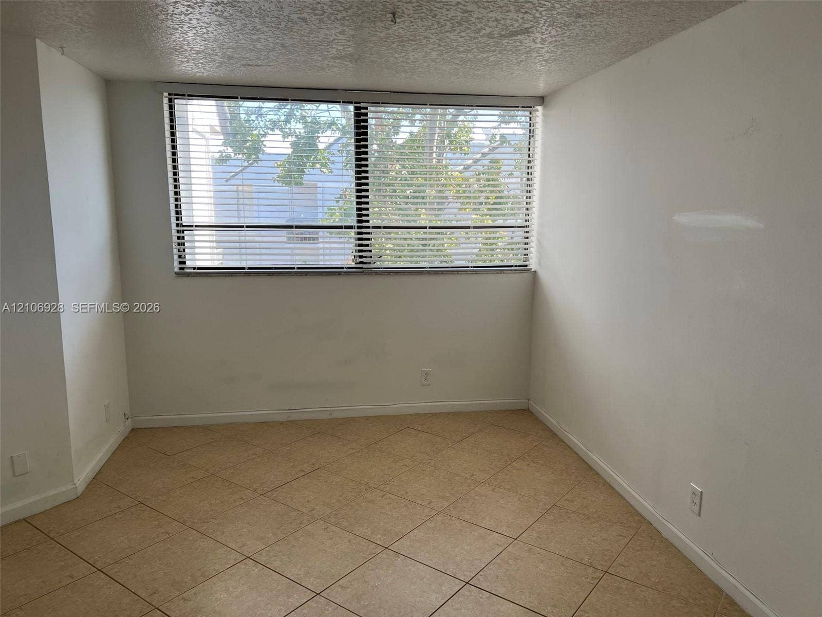 Interior space featuring large-format ceramic tile flooring, neutral wall finishes, and a wide window with integrated horizontal blinds