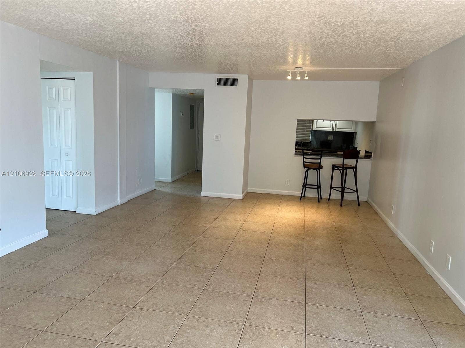 Open-concept interior featuring neutral wall tones, large-format tile flooring, a pass-through opening, and dual-panel closet doors