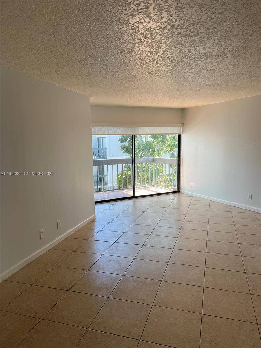 Living area featuring large-format tile flooring, textured ceilings, and a sliding glass door providing access to a private balcony