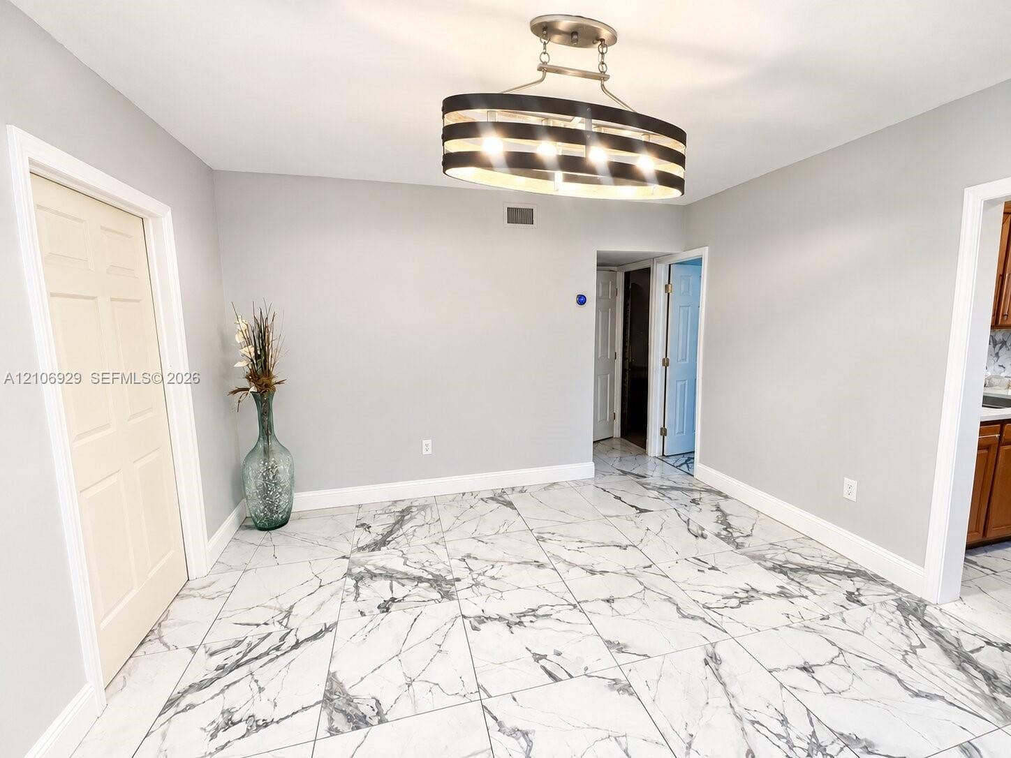 12700 Wood Street, Miami, FL 33167 Large-format tile flooring featuring high-contrast veining, complemented by an oval-profile multi-light pendant fixture with a dark metallic finish and six-panel interior doors