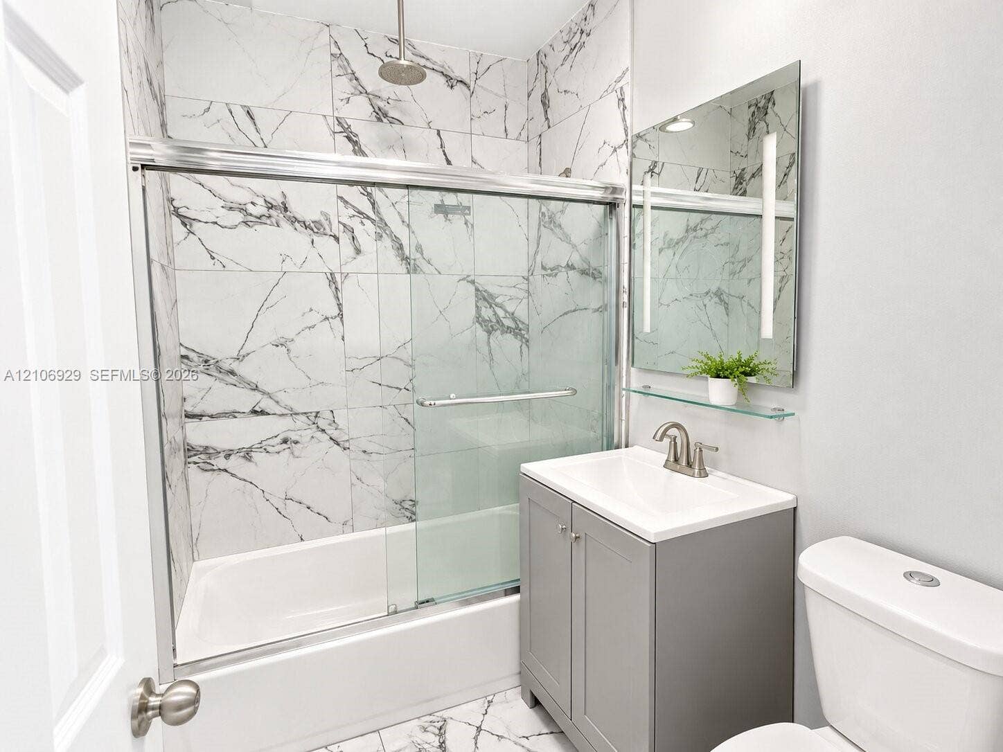 12700 Wood Street, Miami, FL 33167 Bathroom featuring floor-to-ceiling veined tile, glass shower enclosure with chrome hardware, rain-style showerhead, vanity with integrated sink, and wall-mounted mirror