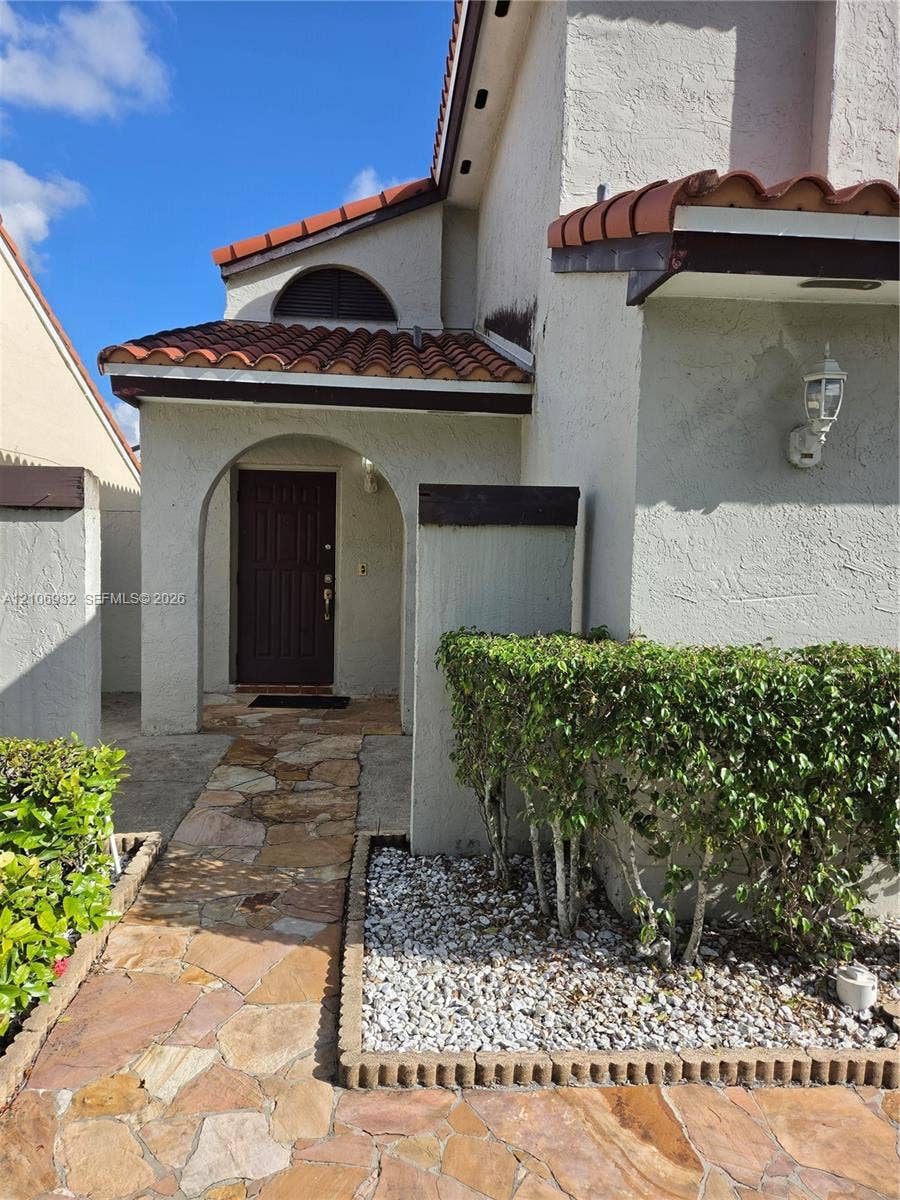 6328 NW 181st Terrace, Hialeah, FL 33015 Stucco exterior featuring a covered entryway with a terracotta-style tiled roof, arched architectural details, and natural stone paver walkway