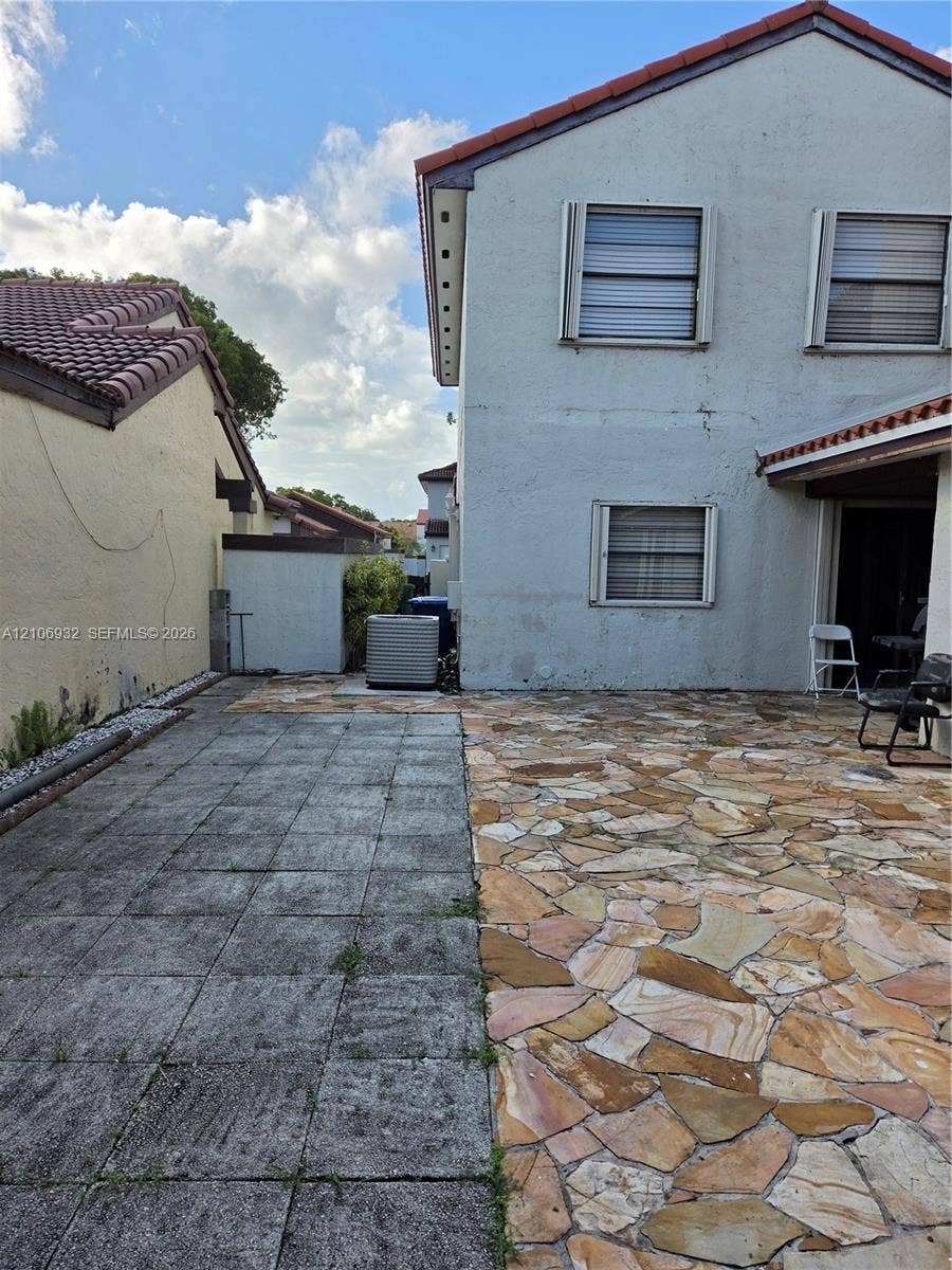 6328 NW 181st Terrace, Hialeah, FL 33015 Exterior patio area featuring a combination of rectangular concrete pavers and natural stone flagstone surfacing, paired with a stucco-finish building facade, tiled roofline, and window shutters