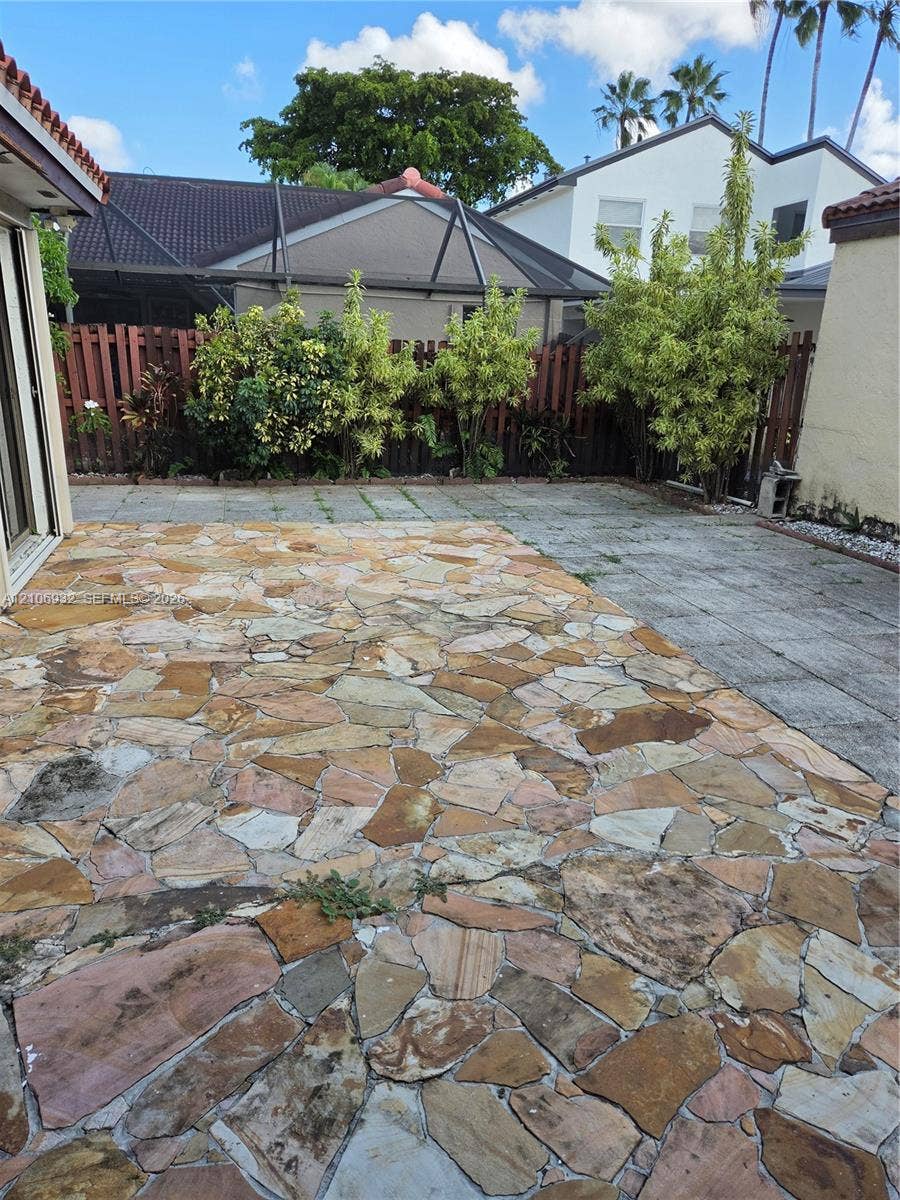 6328 NW 181st Terrace, Hialeah, FL 33015 Flagstone patio featuring a concrete paved section, enclosed by wood privacy fencing and mature landscaping