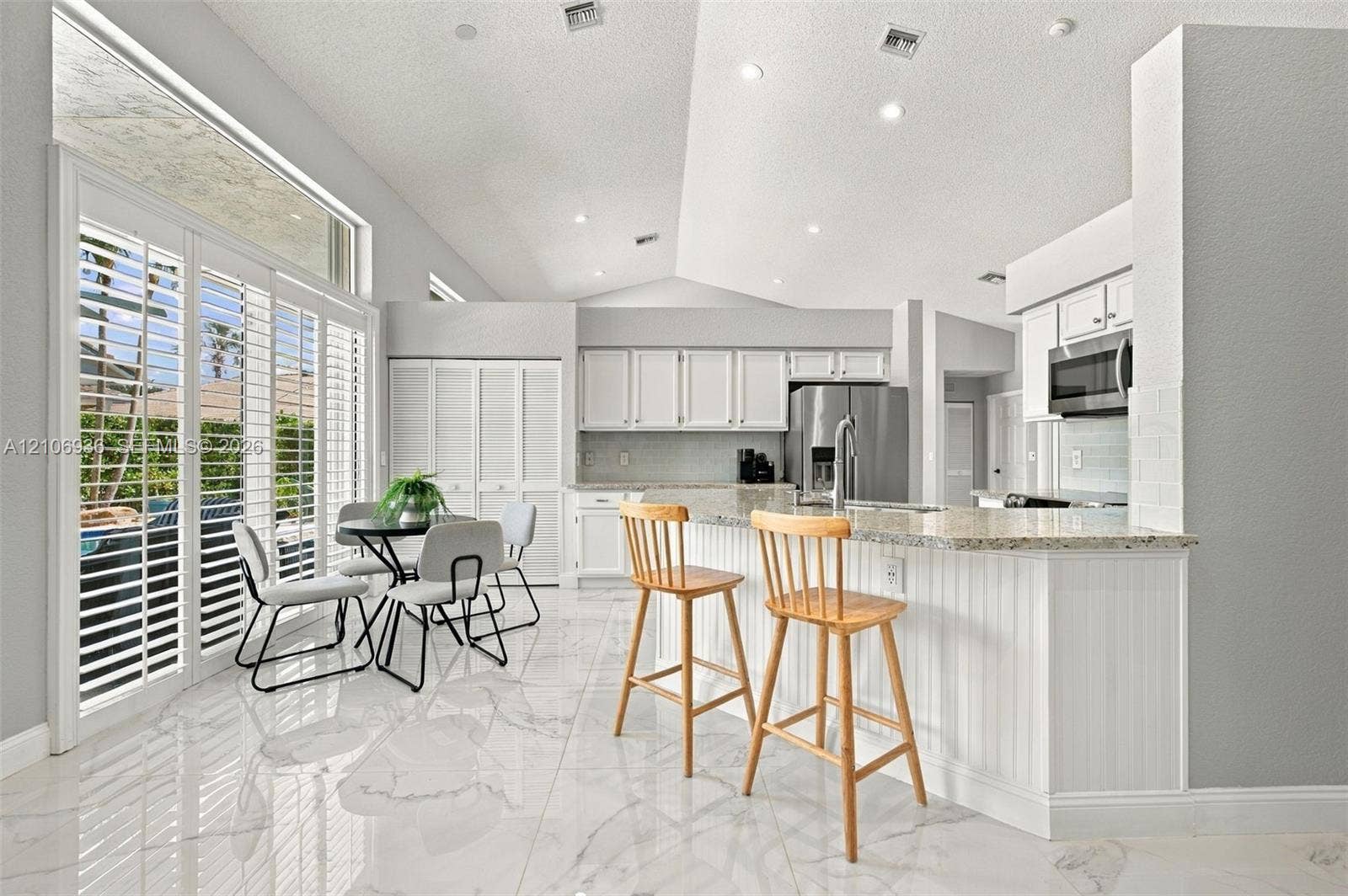 Kitchen featuring vaulted ceilings, stone-surface countertops, beadboard cabinet detailing, large-format tile flooring, and floor-to-ceiling sliding glass doors with plantation shutters