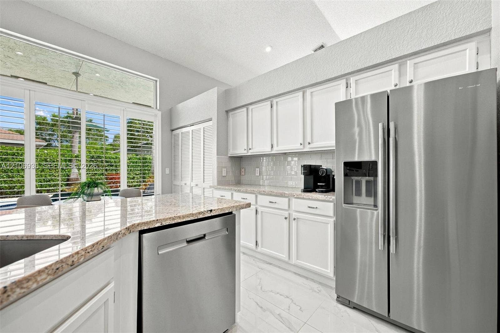 Kitchen featuring white cabinetry, stone-finish countertops, stainless steel appliances, tile flooring, and large windows with transom panels