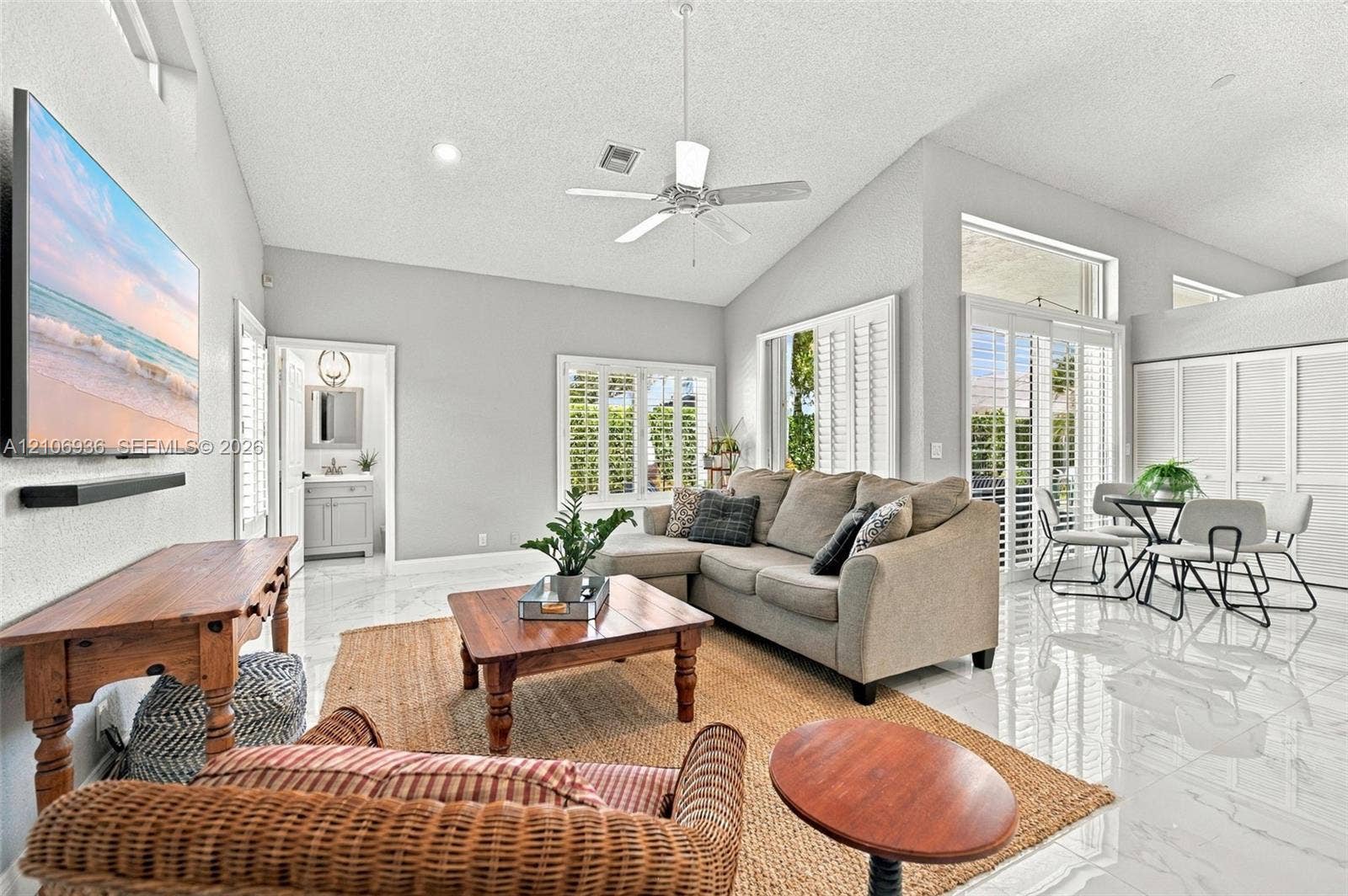 Living area featuring vaulted ceilings, polished tile flooring, plantation shutters, and a ceiling fan