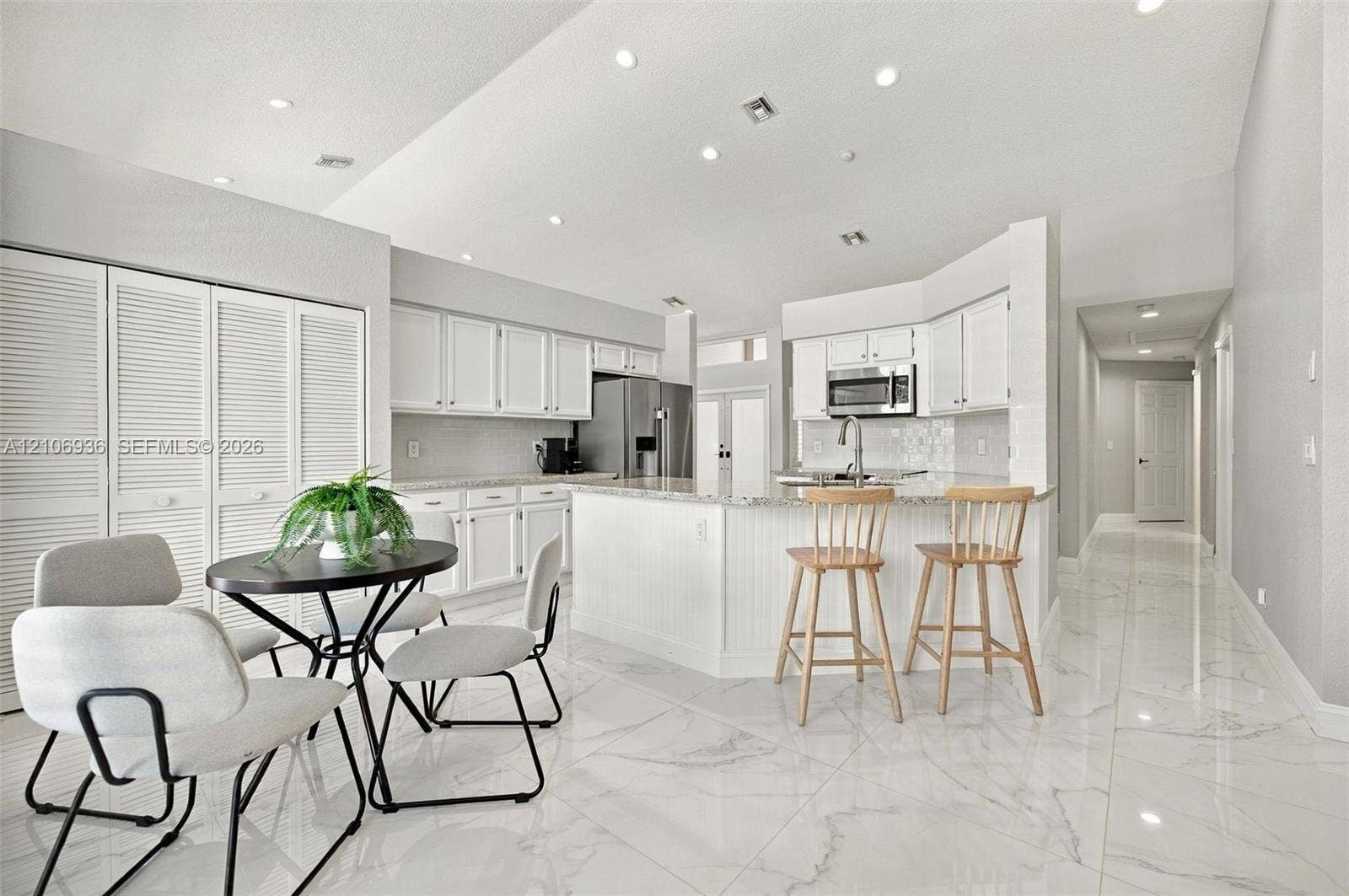 Kitchen featuring white cabinetry, stone-finish countertops, stainless steel appliances, a center island with bar seating, and large-format porcelain tile flooring