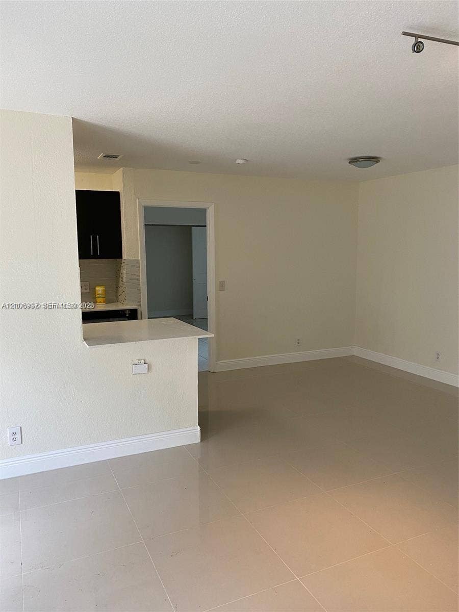 Open-concept area featuring light-colored tile flooring, a kitchen pass-through counter with a solid surface top, and dark wood-finish cabinetry