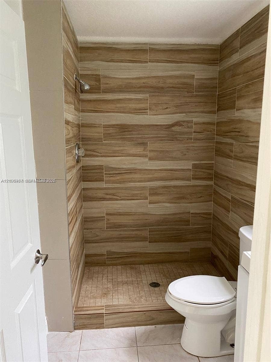 Walk-in shower featuring wood-finish tile wall surround, integrated tiled shower pan, and chrome fixtures