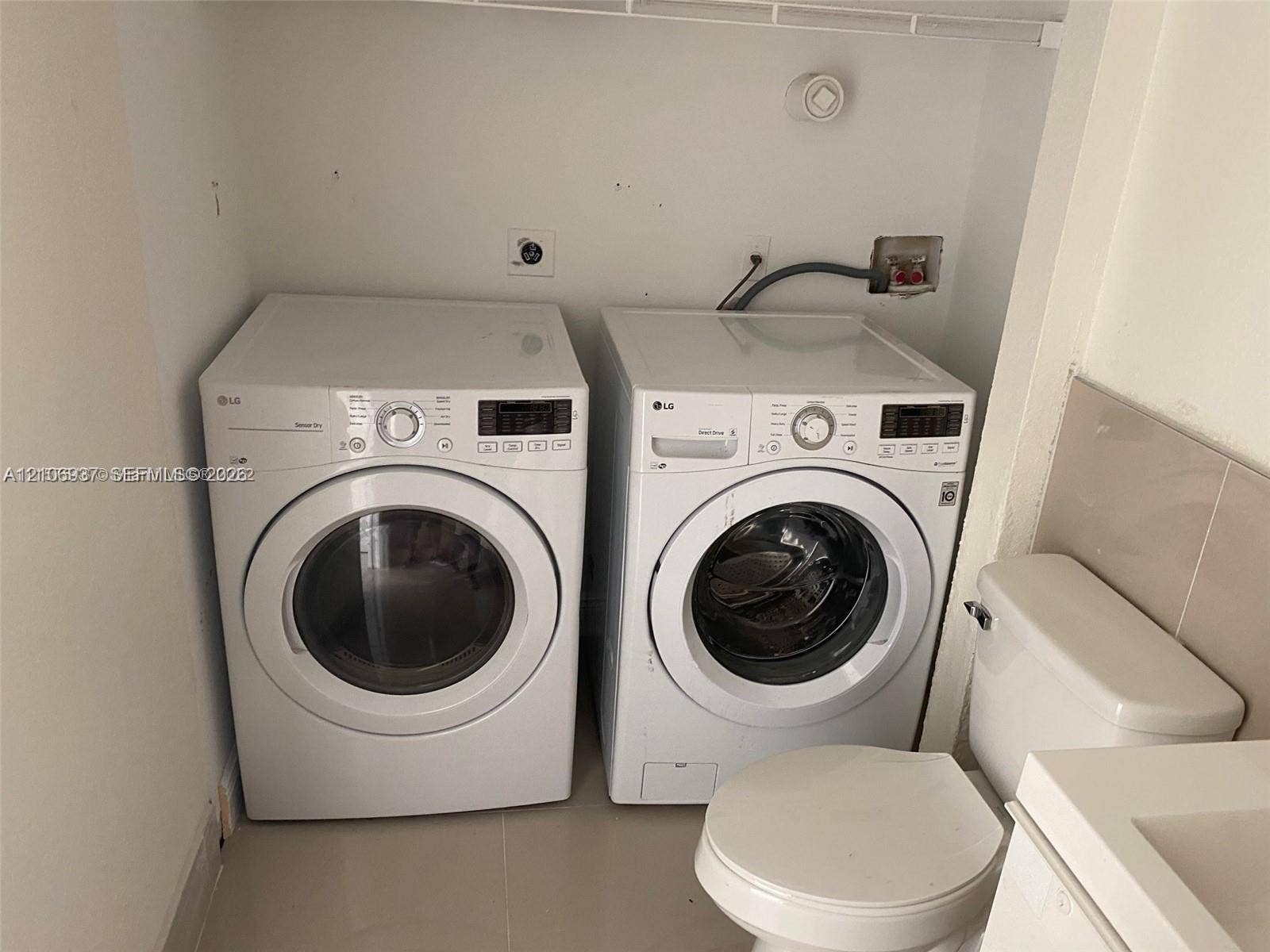 Utility area featuring side-by-side white front-loading appliances, ceramic tile flooring, a standard toilet, and a built-in vanity sink