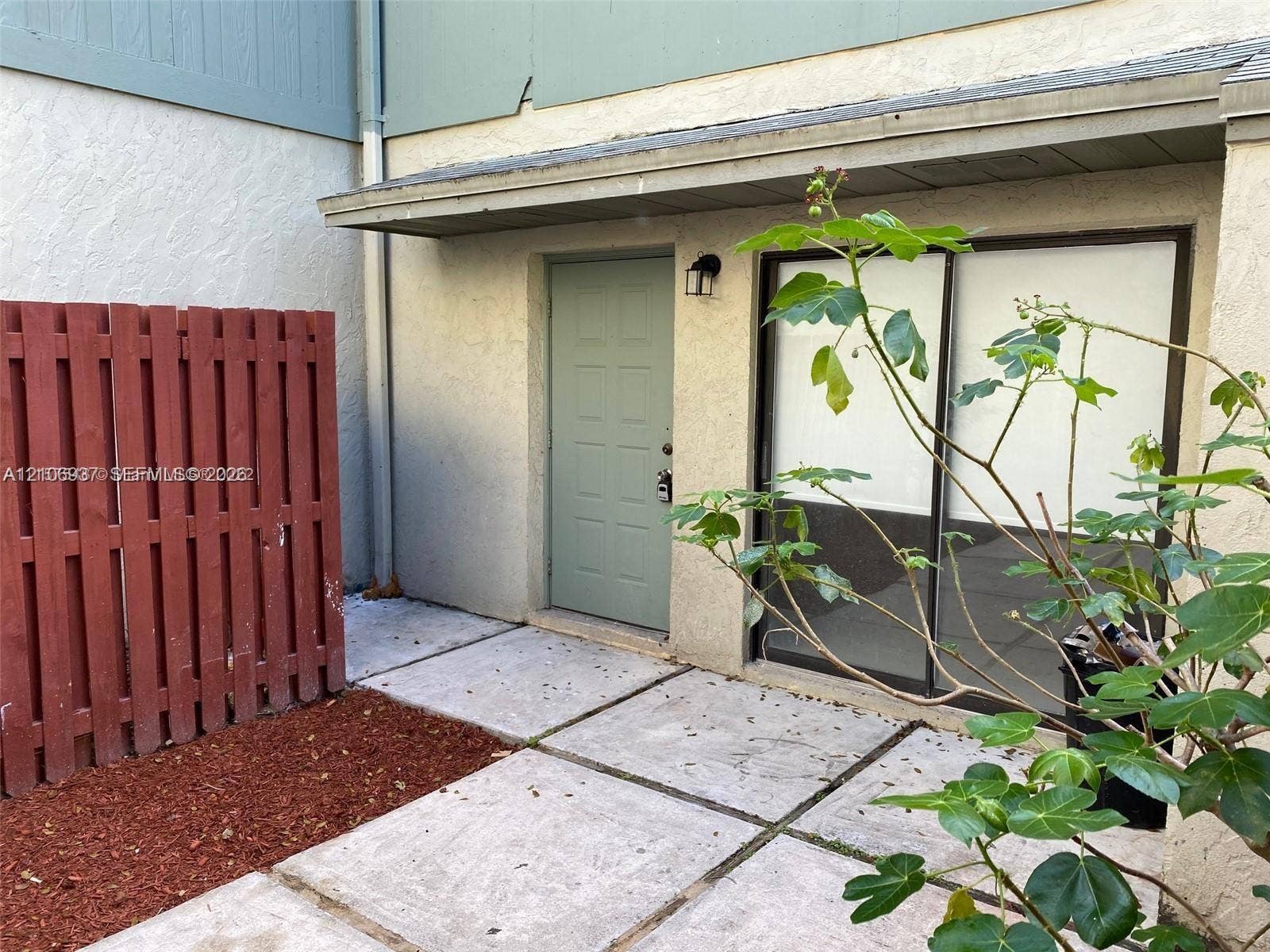 Private patio area featuring concrete paver flooring, a red-painted wood fence, sliding glass door, and exterior sconce lighting