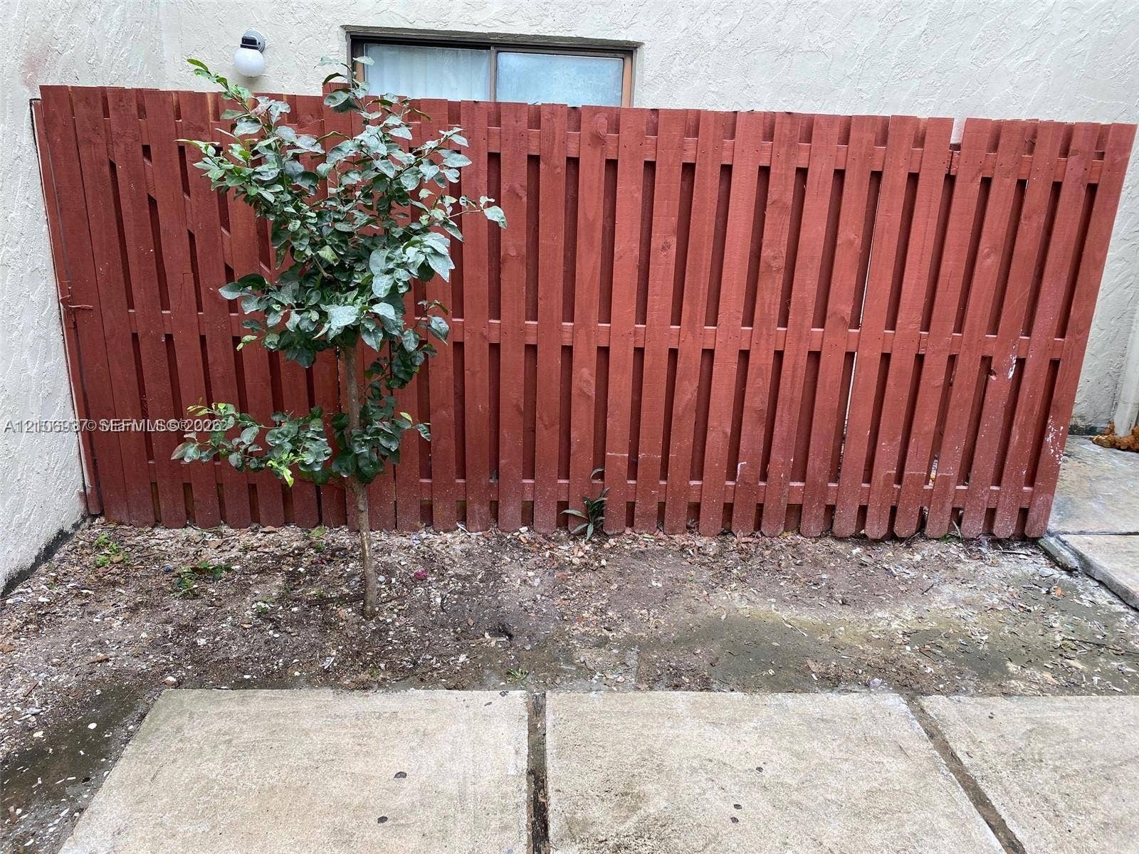 Stucco exterior wall featuring a solid wood-plank privacy fence, concrete paver patio, and exterior wall-mounted lighting