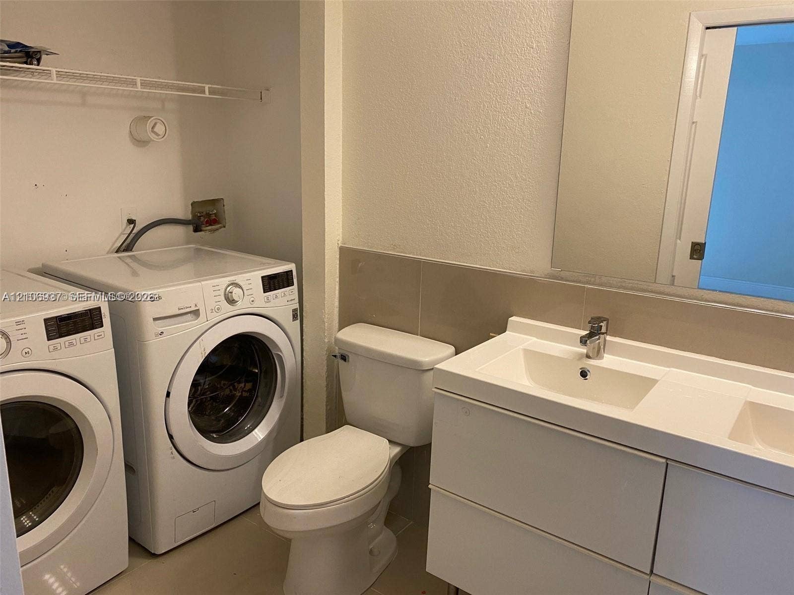 Modern floating vanity with a double-basin rectangular sink, polished chrome fixtures, and a wall-to-wall mirror, featuring a floor-mounted toilet and built-in laundry area with overhead shelving