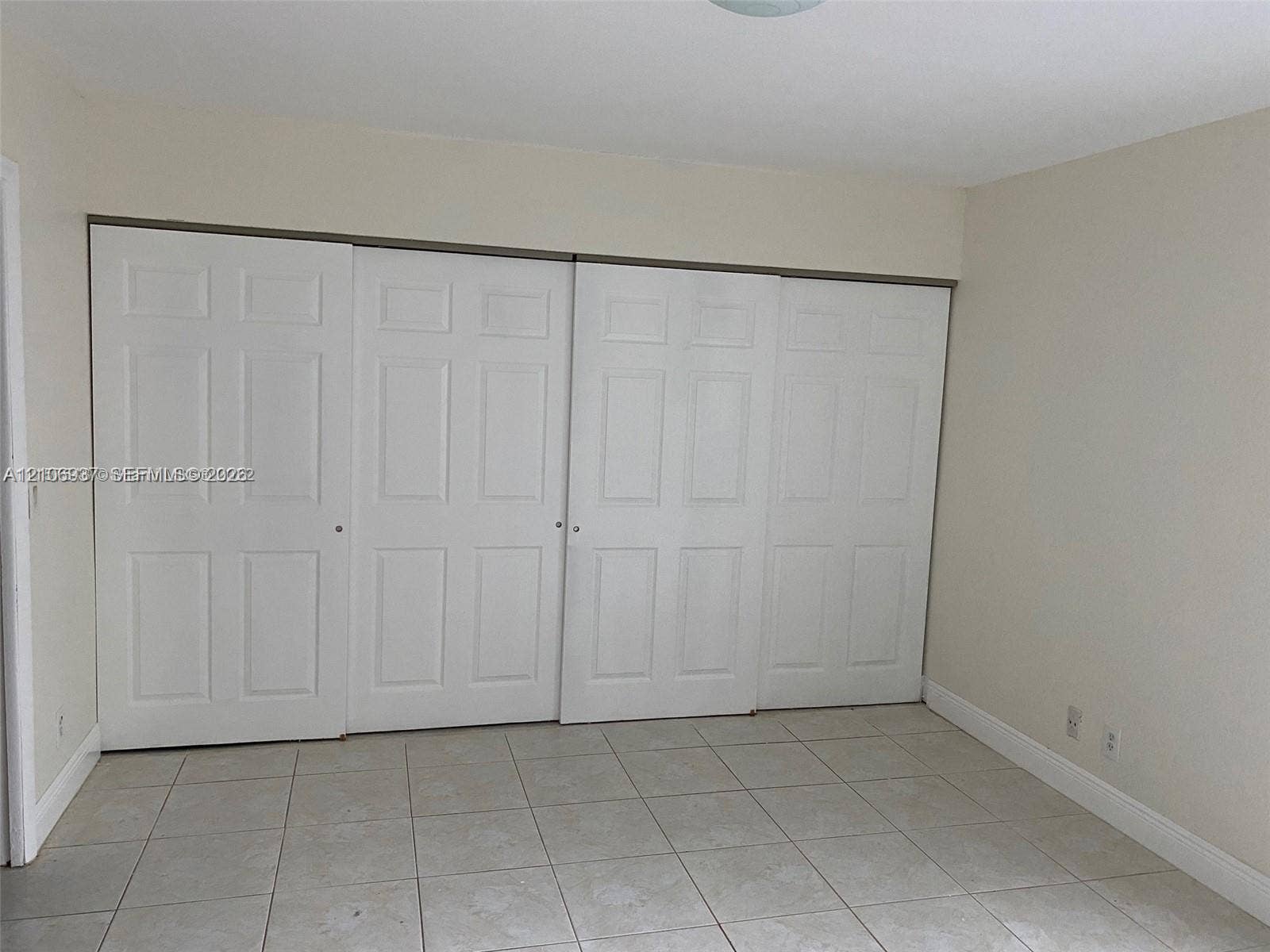 Room interior featuring large quadruple-panel sliding closet doors with classic raised-panel detailing and neutral ceramic tile flooring