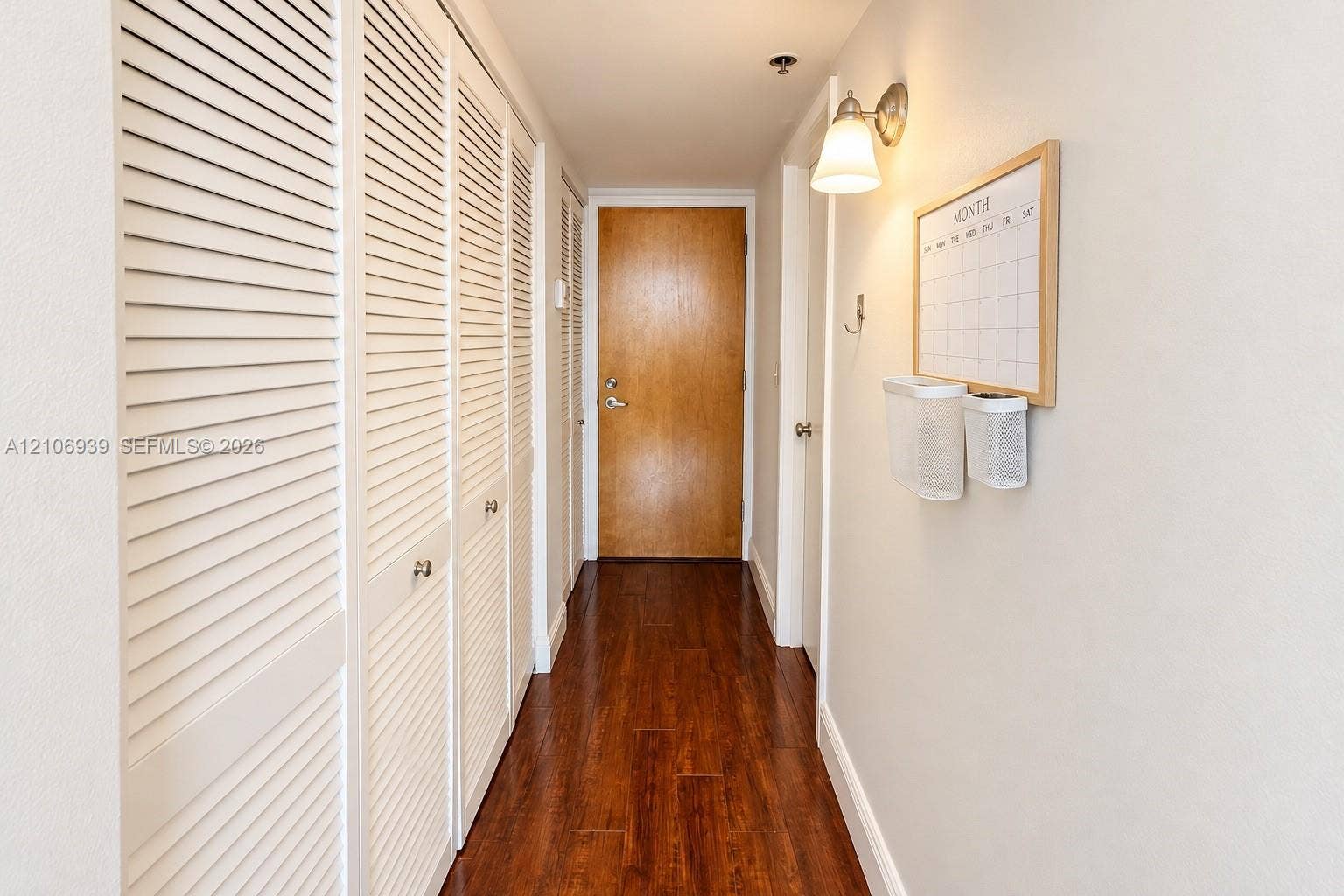 7601 E Treasure Drive, #802, North Bay Village, North Bay Village, FL 33141 Hallway featuring wood-finish flooring, white louvered closet doors, and wall-mounted light fixture