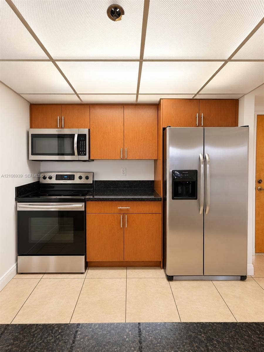7601 E Treasure Drive, #802, North Bay Village, North Bay Village, FL 33141 Kitchen featuring flat-panel wood-finish cabinetry, dark solid-surface countertops, stainless steel appliances, and large-format tile flooring