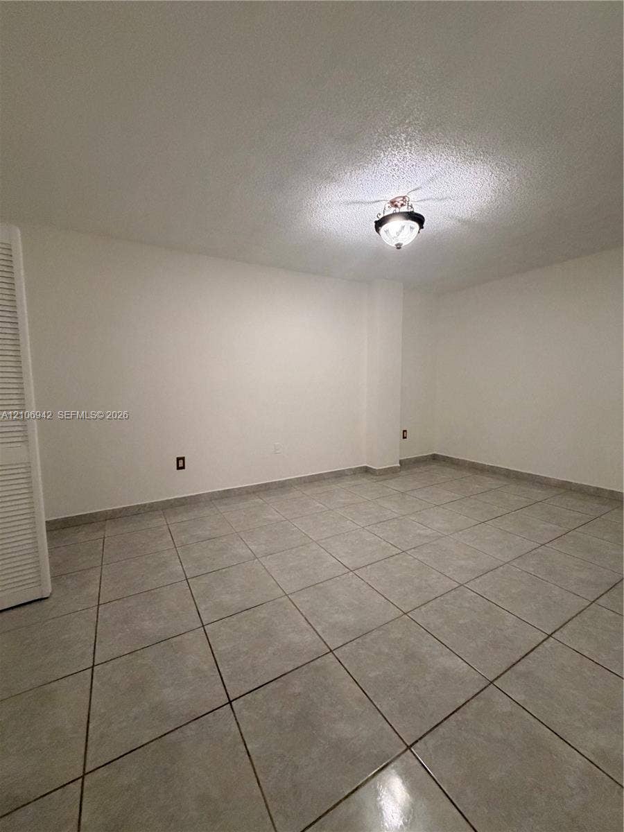 Neutral-tone tile flooring, white wall finishes, and louvered-style closet doors with a ceiling-mounted light fixture