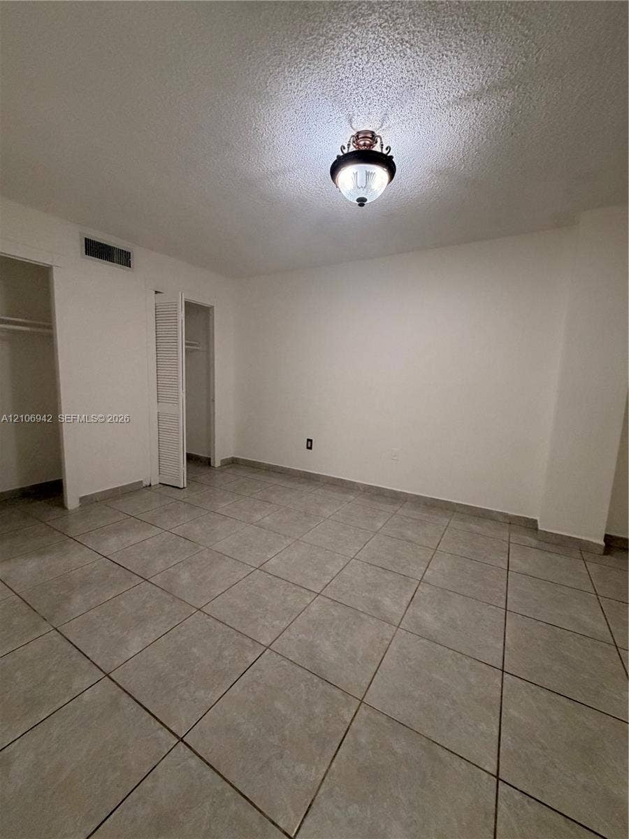 Interior room featuring large-format ceramic tile flooring, neutral wall finishes, a semi-flush mount light fixture, and two closets with louvered doors