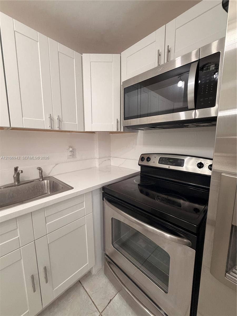 Kitchen featuring white shaker-style cabinetry, solid-surface countertops with a matching backsplash, stainless steel appliances, and an undermount sink