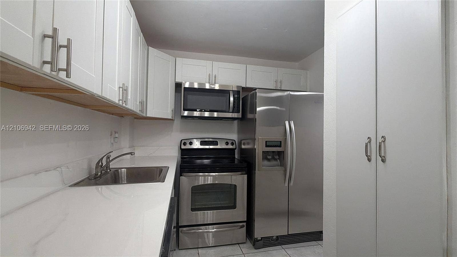 Kitchen featuring white shaker-style cabinetry, solid-surface countertops, stainless steel appliances, and a tall floor-to-ceiling built-in pantry