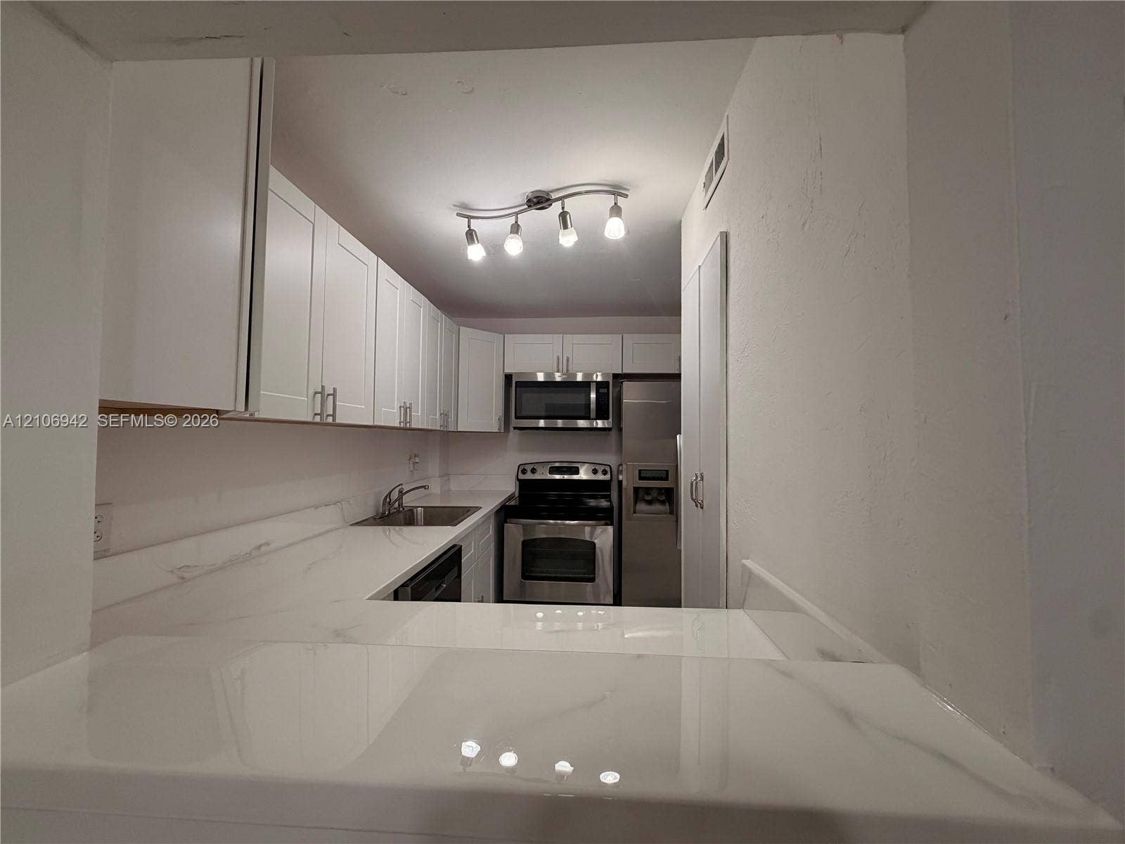 Kitchen featuring white shaker-style cabinetry, stone-finish countertops, stainless steel appliances, and multi-light track lighting