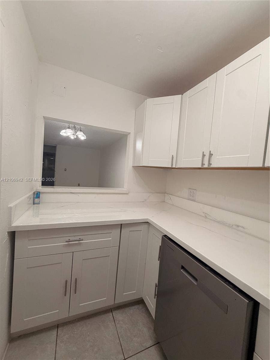 Kitchen featuring white shaker-style cabinetry, stone-finish countertops, tile flooring, and a stainless steel dishwasher