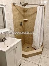 1674 NE 174th Street, #Rear, North Miami Beach, North Miami Beach, FL 33162 Bathroom featuring a white vanity cabinet, ceramic tile flooring, and a corner shower enclosure with neutral-toned wall tile, built-in shelving, and a chrome rainfall showerhead
