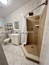 1674 NE 174th Street, #Rear, North Miami Beach, North Miami Beach, FL 33162 Bathroom featuring a tiled stall shower with a fixed showerhead, white vanity cabinet, ceramic tile flooring, and wall-mounted vanity mirror