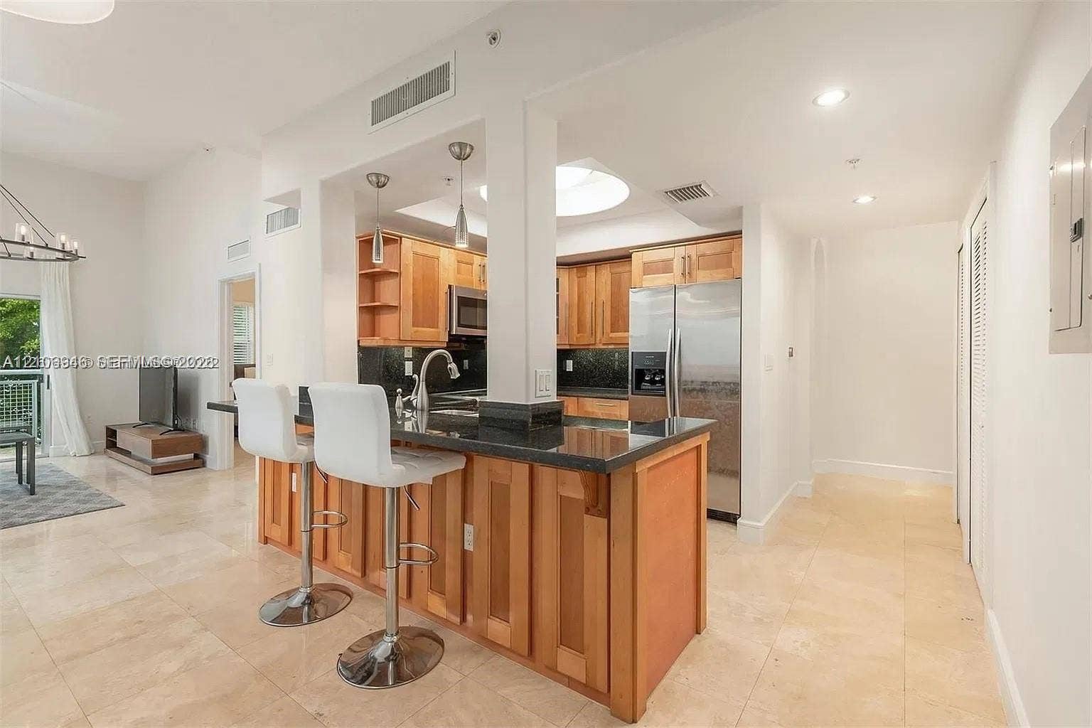 Kitchen featuring natural-finish wood cabinetry, dark stone countertops, stainless steel appliances, a recessed skylight, and stone flooring