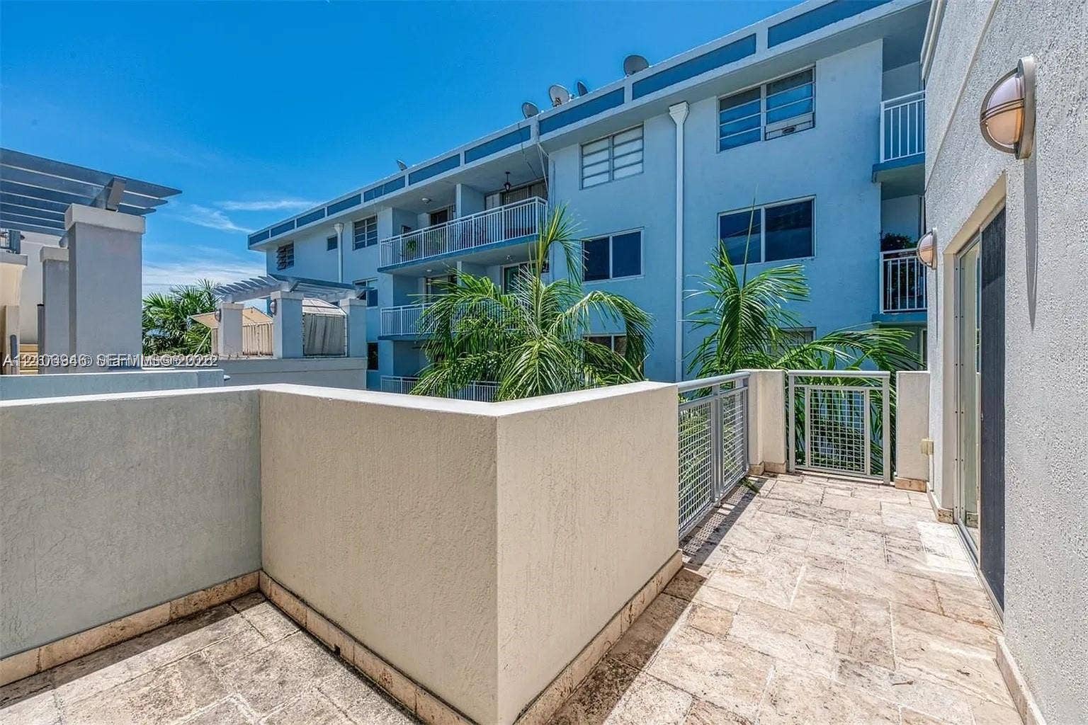 Private terrace featuring stone tile flooring, stucco privacy walls, metal railing, and wall-mounted exterior lighting