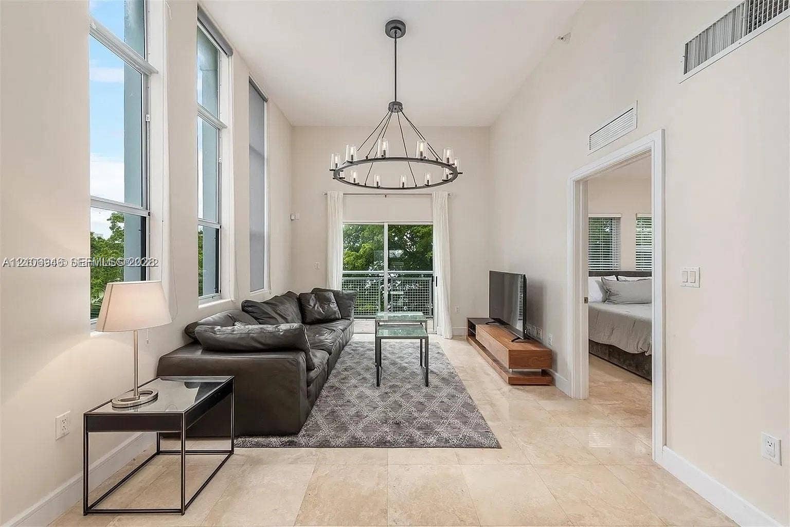 High ceilings with floor-to-ceiling windows, polished stone flooring, and a decorative circular chandelier