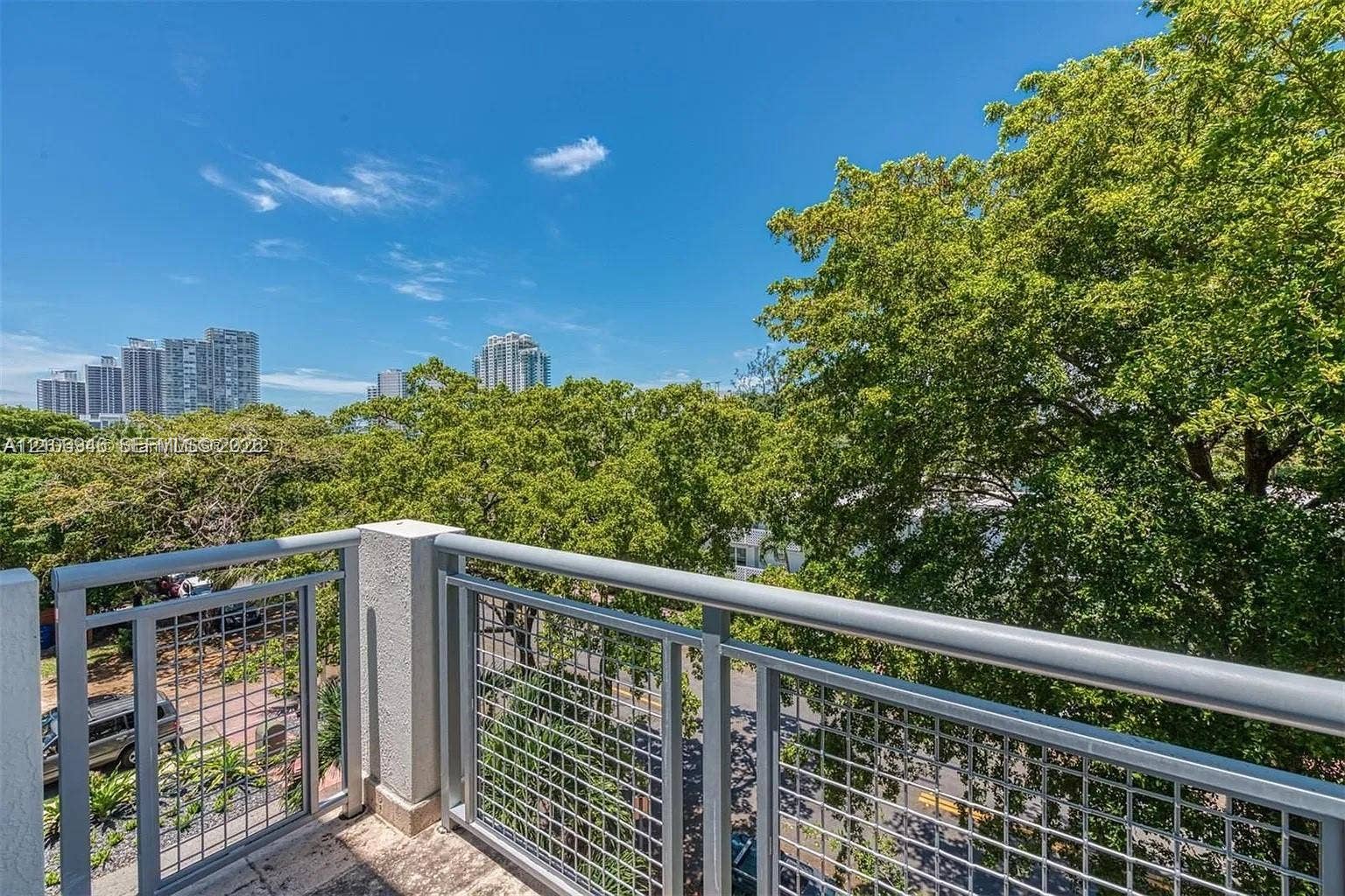 Private balcony with metal mesh railings, concrete flooring, and mature canopy trees