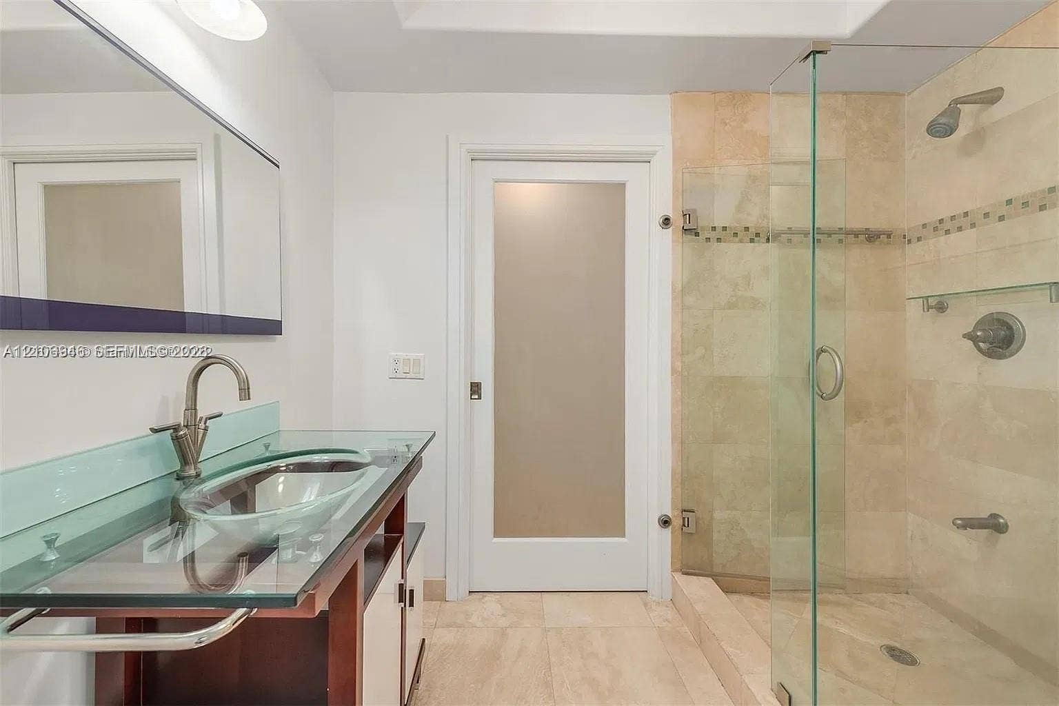 Bathroom featuring a glass-topped vanity with an integrated basin, frosted glass panel door, and a walk-in shower with stone tile surround and frameless glass enclosure