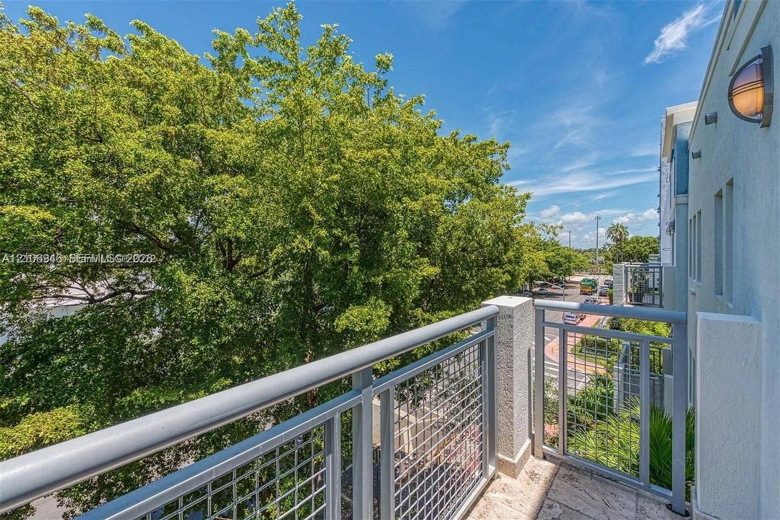 Exterior balcony featuring metal railings with grid-patterned panels, stone flooring, and wall-mounted exterior lighting
