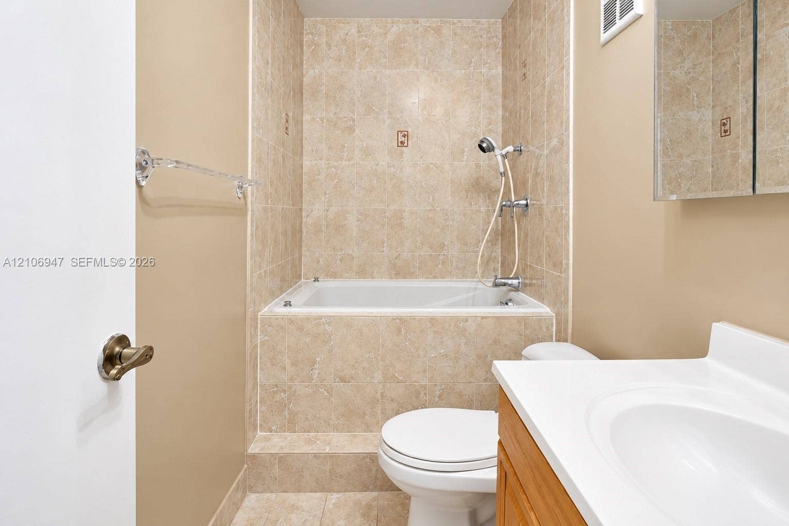 Bathroom featuring a deep-soaking tub with tile surround, wood-finish vanity cabinet, integrated sink, and mirrored medicine cabinet
