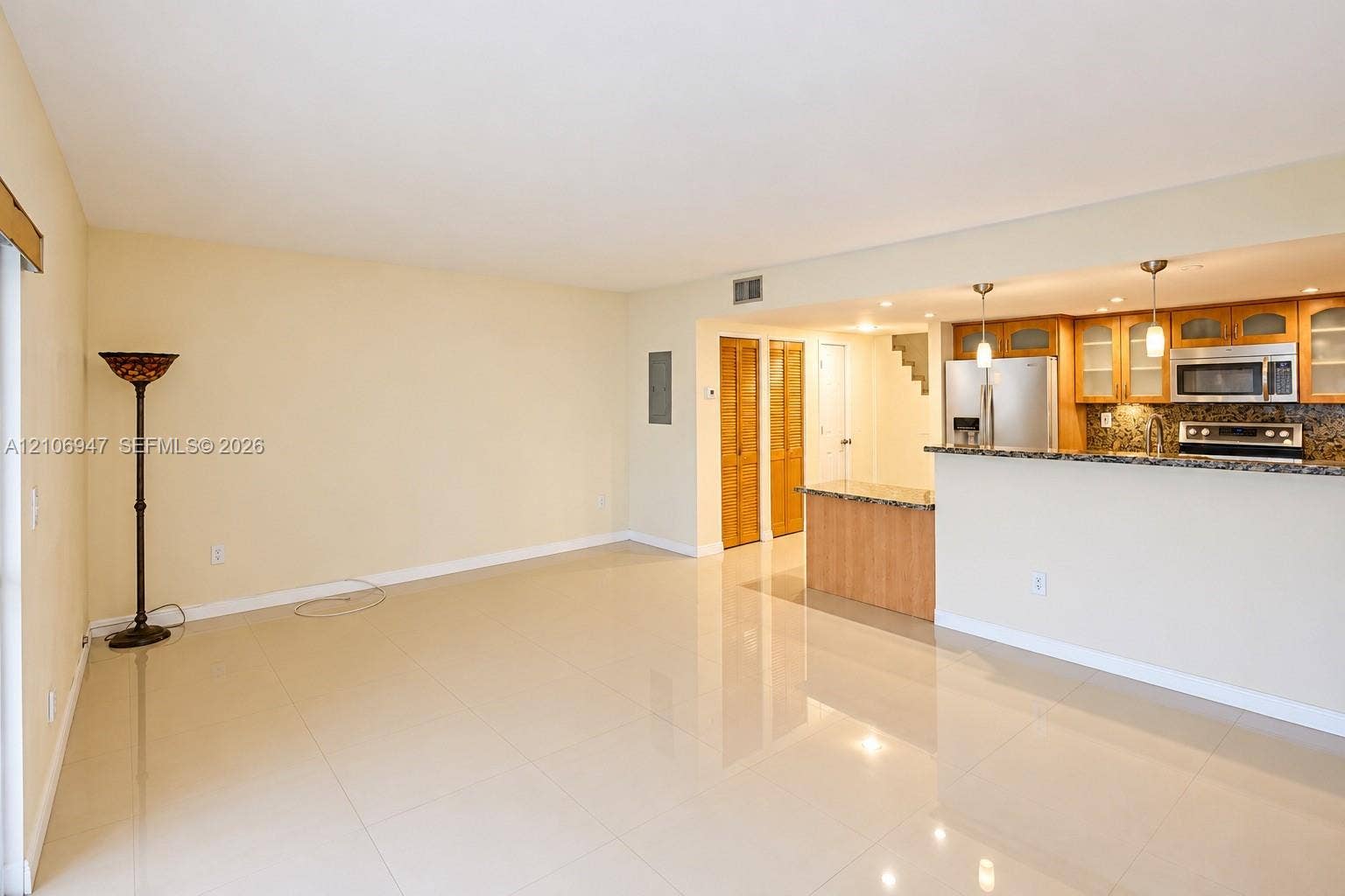 Open-concept area featuring polished tile flooring, kitchen with stone-surfaced peninsula, natural wood cabinetry, stainless steel appliances, and dual pendant light fixtures