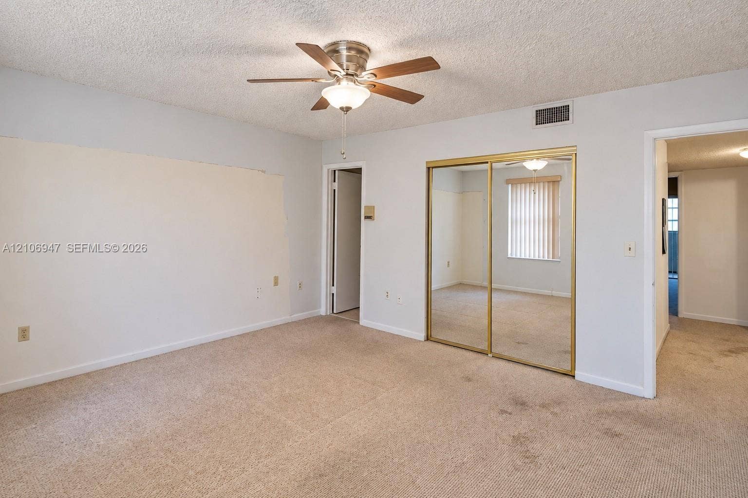 Room featuring neutral wall tones, wall-to-wall carpeting, a ceiling fan with integrated light fixture, and floor-to-ceiling mirrored closet doors with gold-tone frames