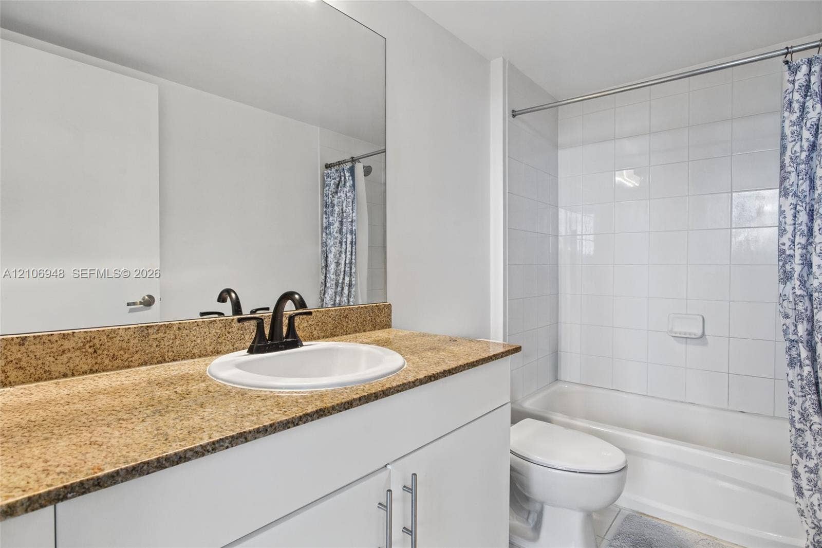 Bathroom featuring a vanity with a stone-finish countertop, undermount sink, dark-finish hardware, full-width mirror, and a tub-shower combination with white wall tile