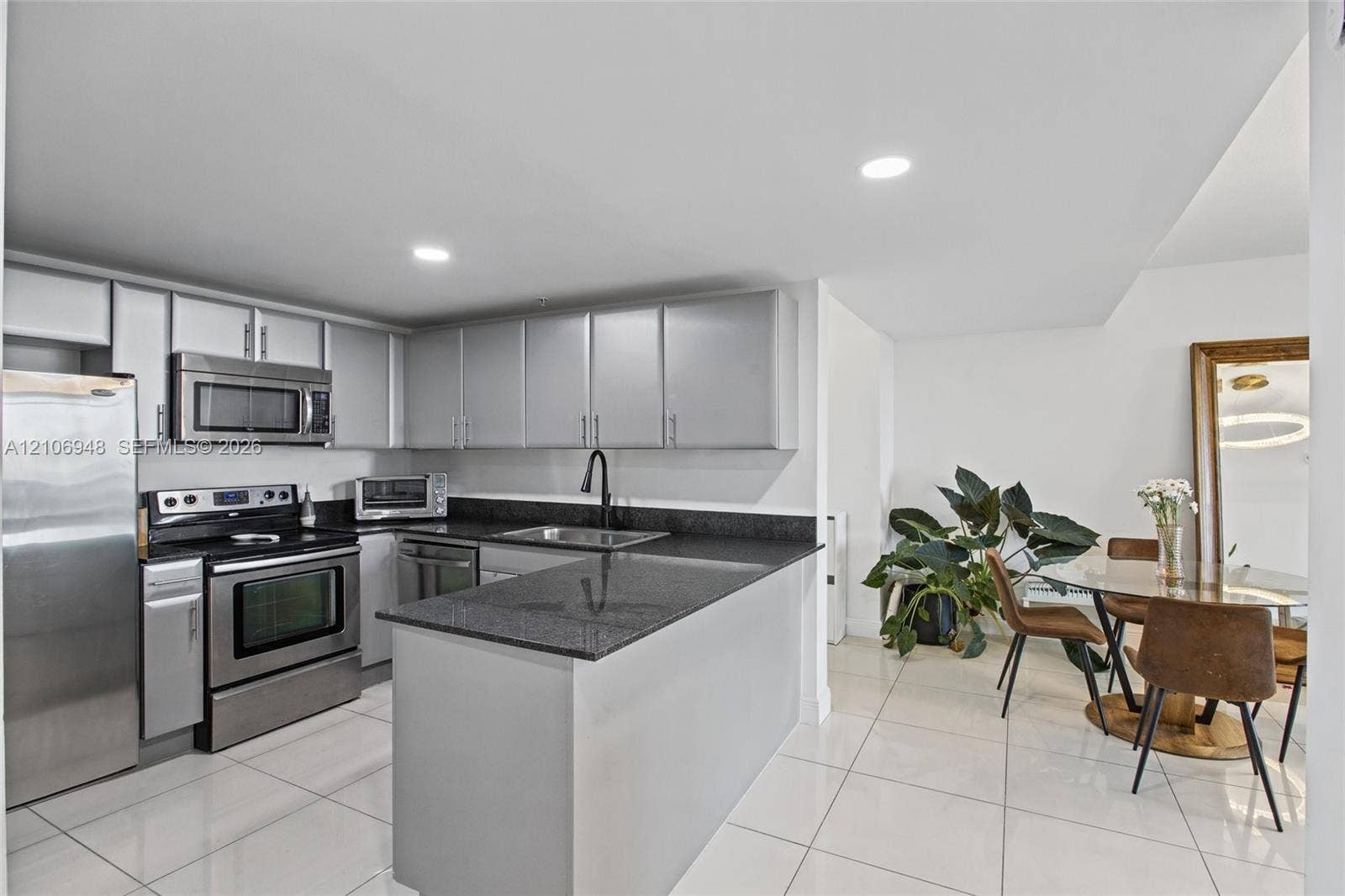 Kitchen featuring stainless steel appliances, dark stone countertops, flat-panel cabinetry, a matte black faucet, and light-toned tile flooring