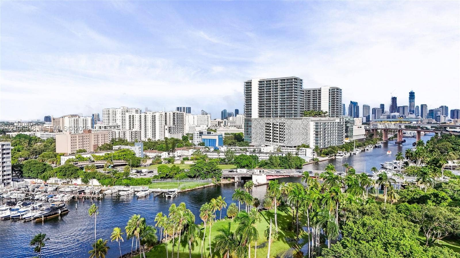 Waterfront properties featuring multiple boat slips, surrounded by dense tropical foliage, with a prominent city skyline in the background