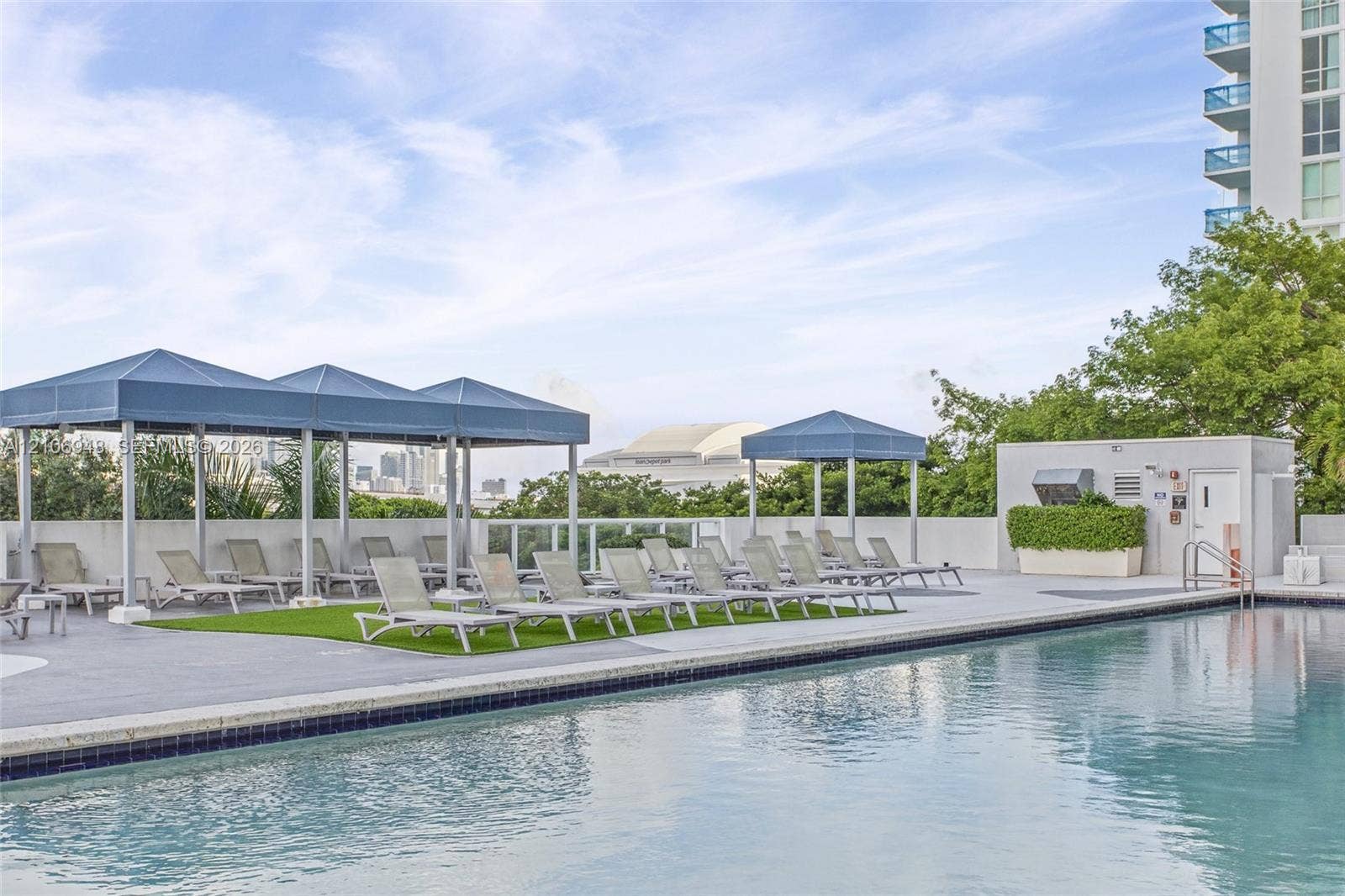 Outdoor swimming pool with tiled border and stone-paved deck, featuring integrated fabric-covered cabanas and maintained landscaping