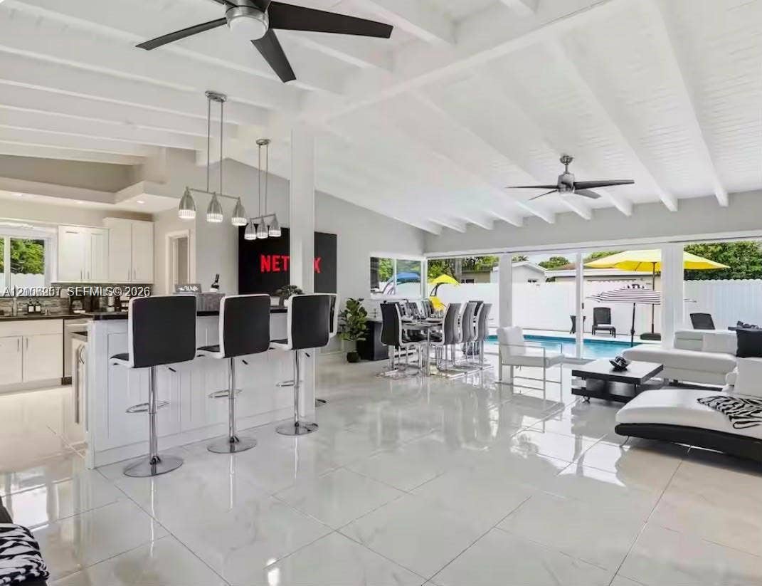 Open-concept interior featuring vaulted, beamed ceilings, oversized tile flooring, a kitchen island with stone countertops, and multiple sliding glass doors