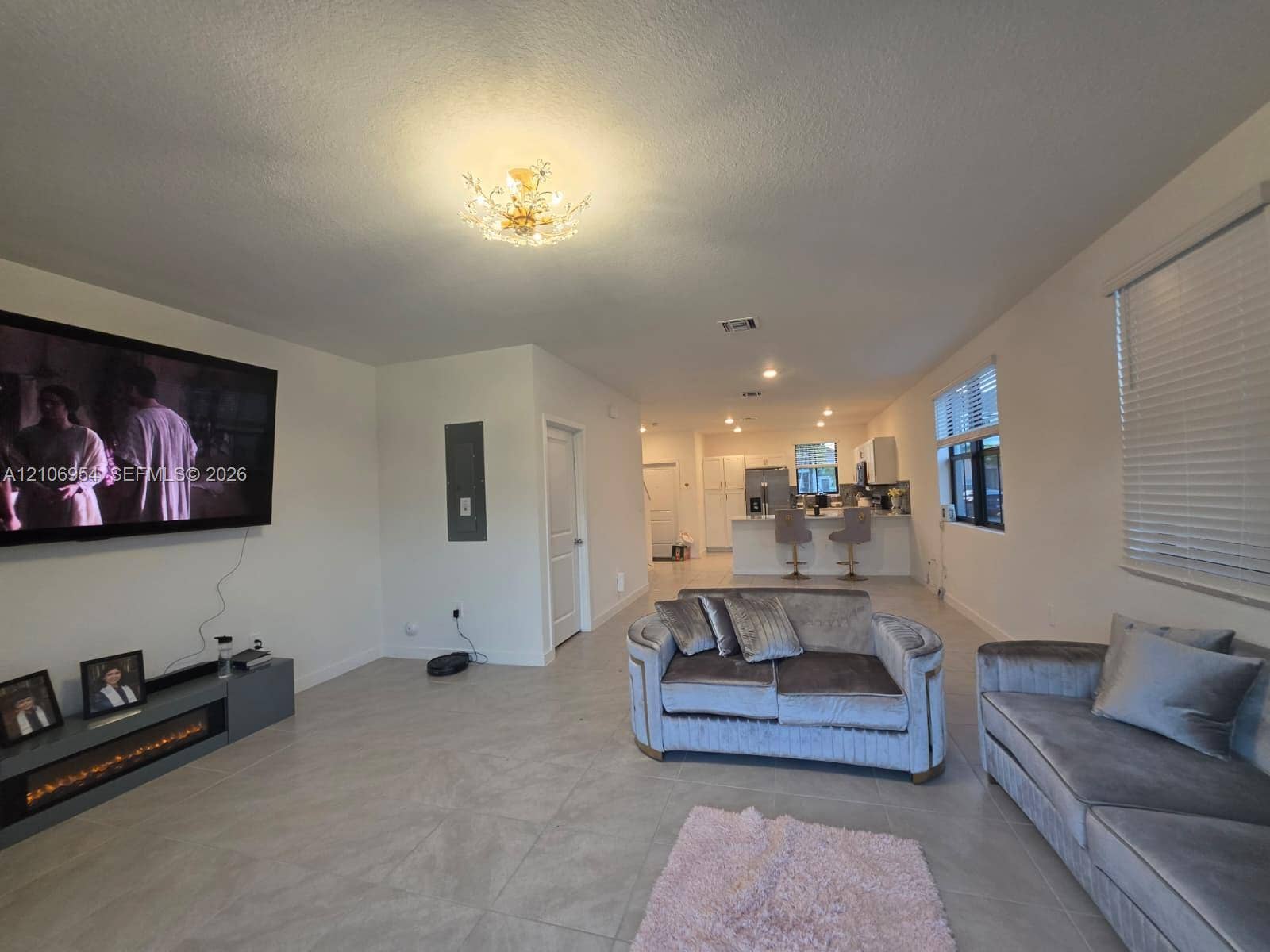 Neutral-toned tile flooring, recessed lighting, decorative flush-mount ceiling fixture, and built-in electric fireplace unit with integrated shelving