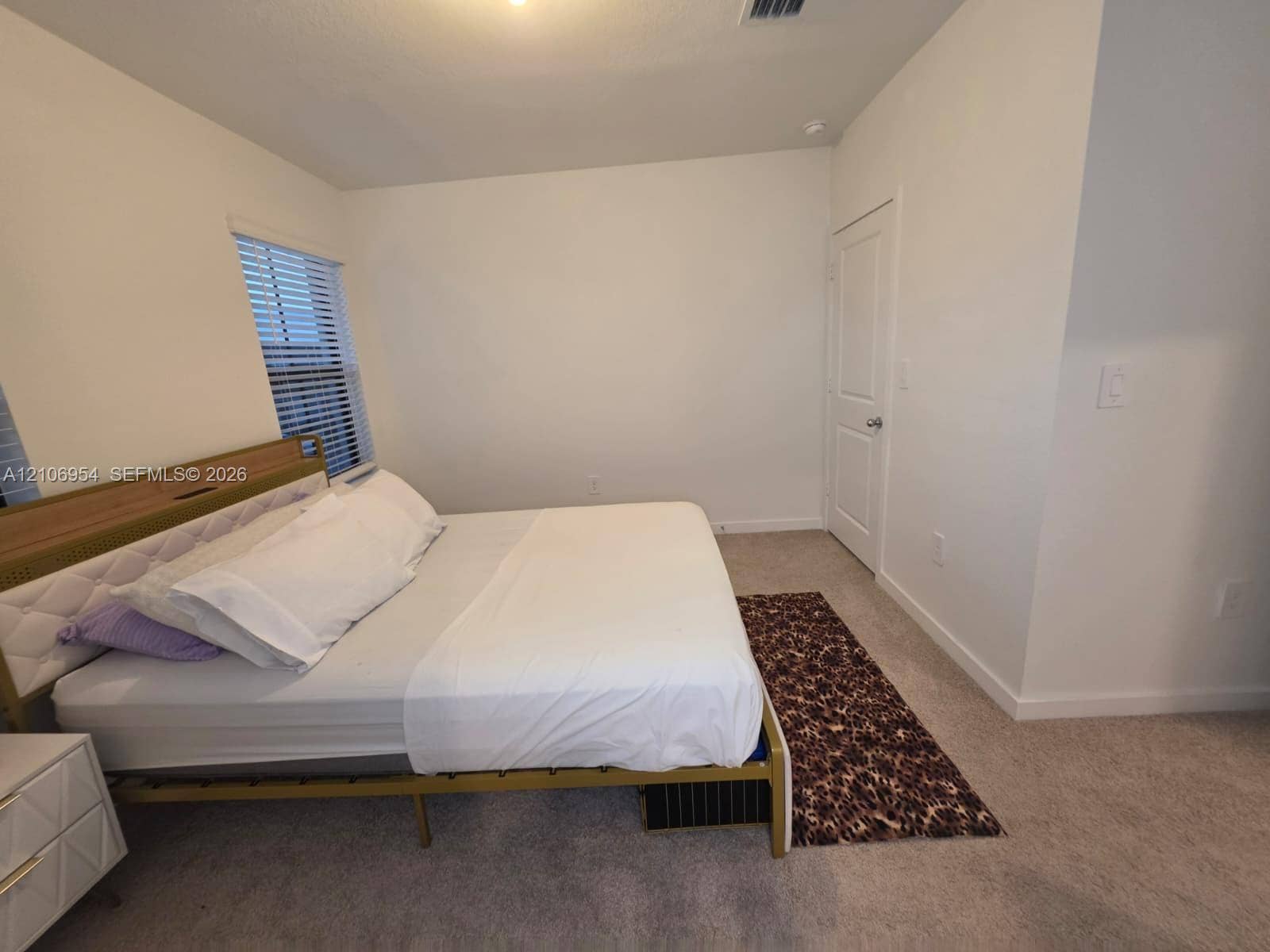 Neutral-toned carpeted flooring, two-panel interior door, and window with horizontal blinds