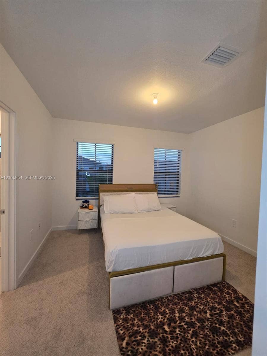 Neutral-toned interior space featuring light-colored wall-to-wall carpeting, two dual-pane windows, and minimalist ceiling-mounted lighting