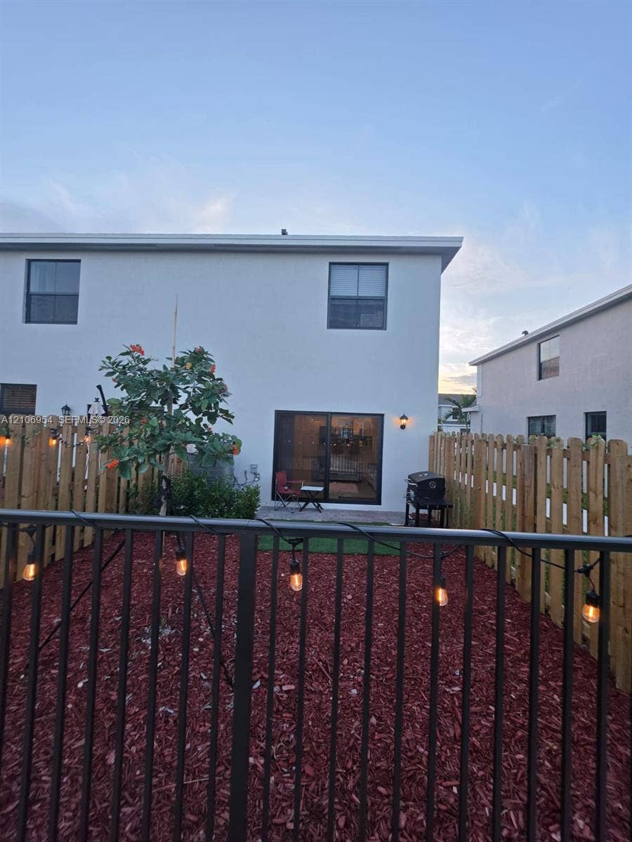 Fenced backyard featuring wood-tone privacy screening, black metal perimeter railing, red-toned mulch ground cover, and sliding glass doors