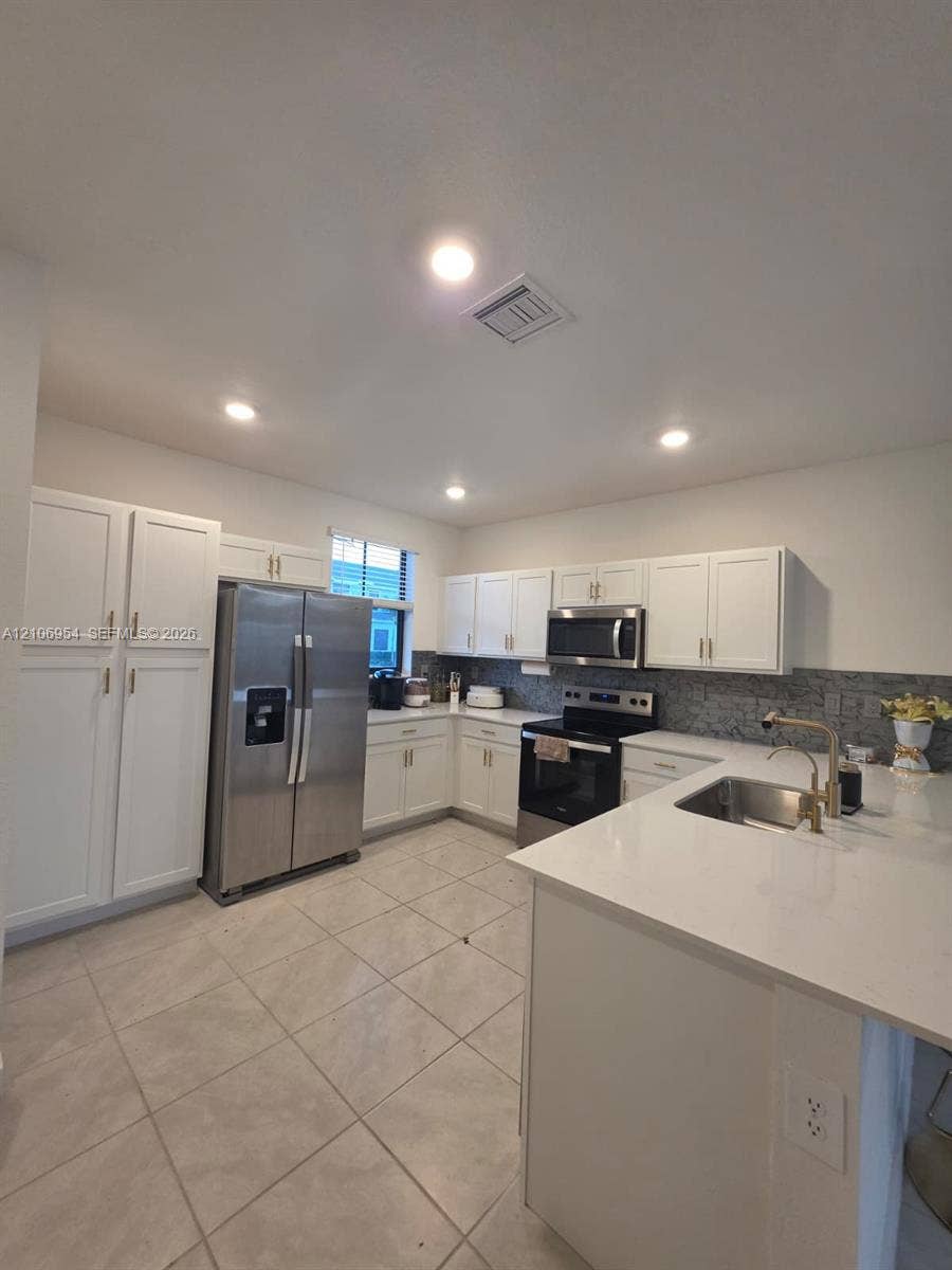 Kitchen featuring white cabinetry, solid-surface countertops, tile flooring, recessed lighting, and stainless steel appliances