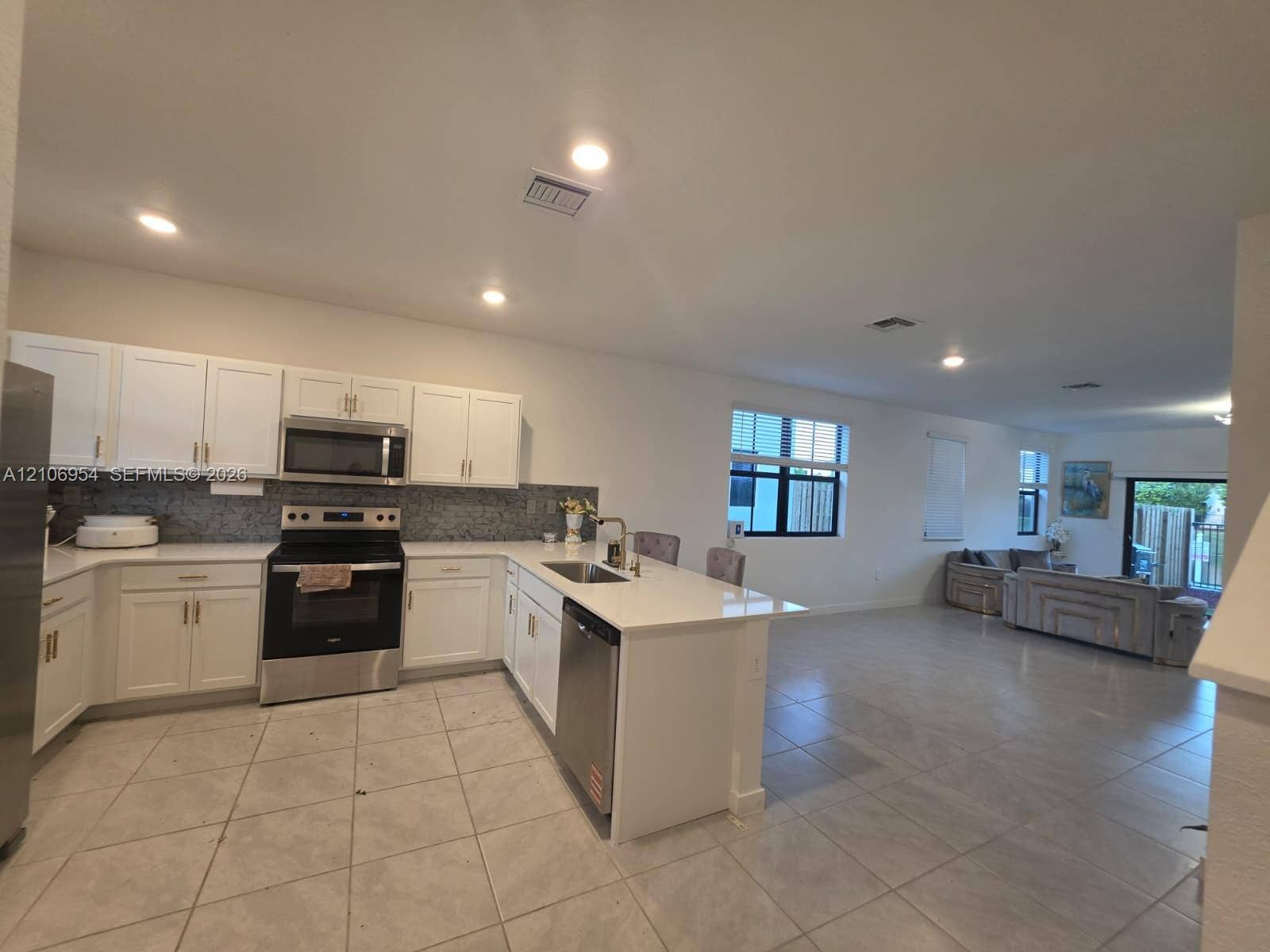 Kitchen featuring white cabinetry, solid-surface countertops, tile backsplash, stainless steel appliances, and a central island with an integrated sink